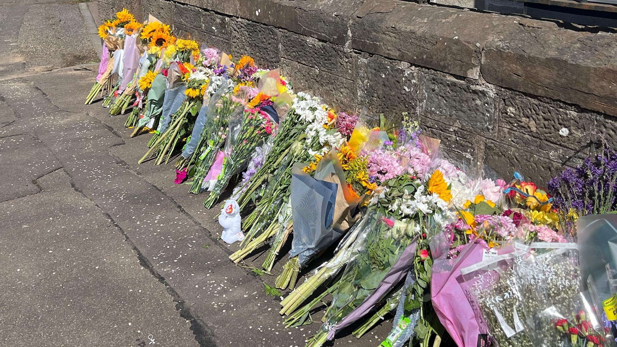 Bunches of flowers in a long line on a pavement near the scene of the incident
