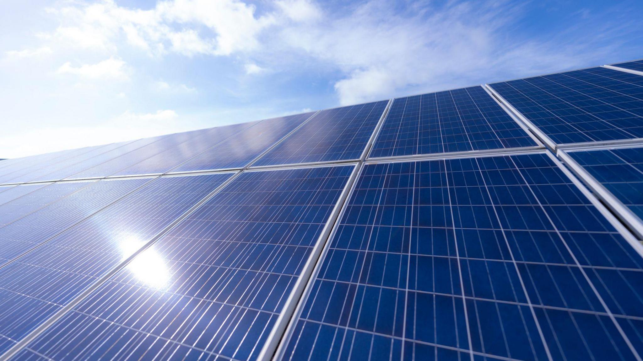 A generic picture of solar panels, with the Sun shining on it.