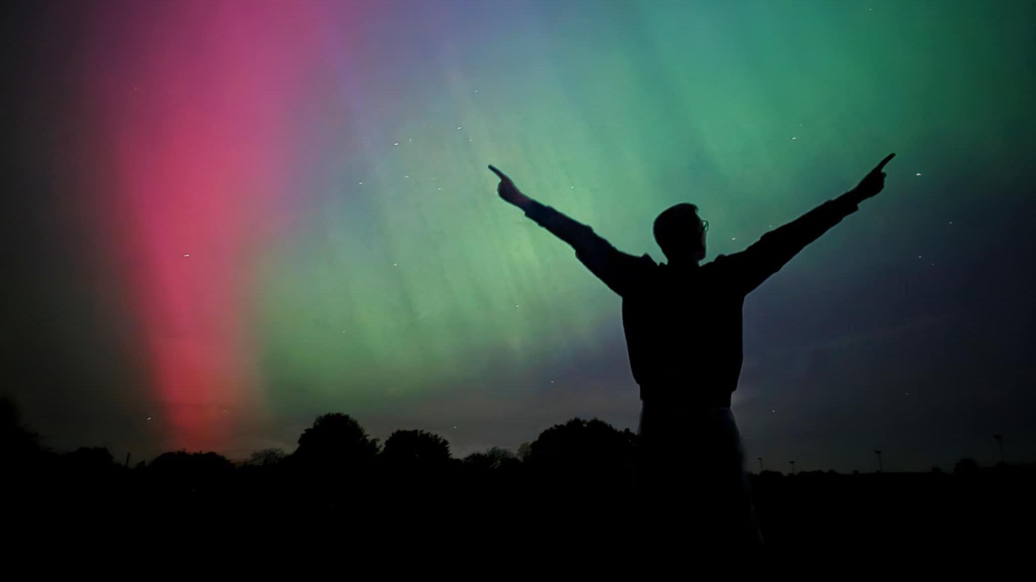 The silhouette of a man can be seen against a backdrop of a pink and green aurora