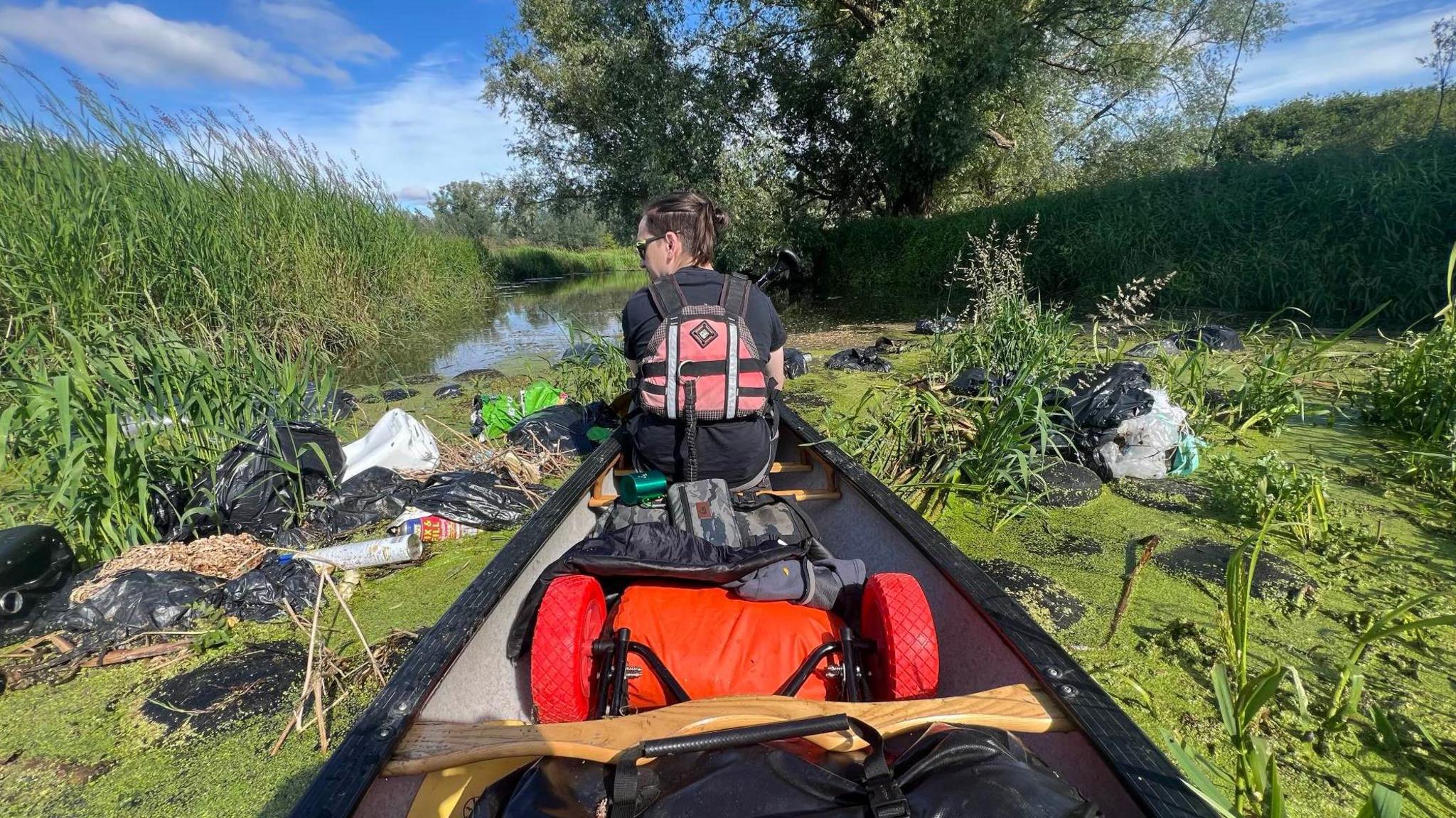 A boat travelling past the rubbish in the River Waveney