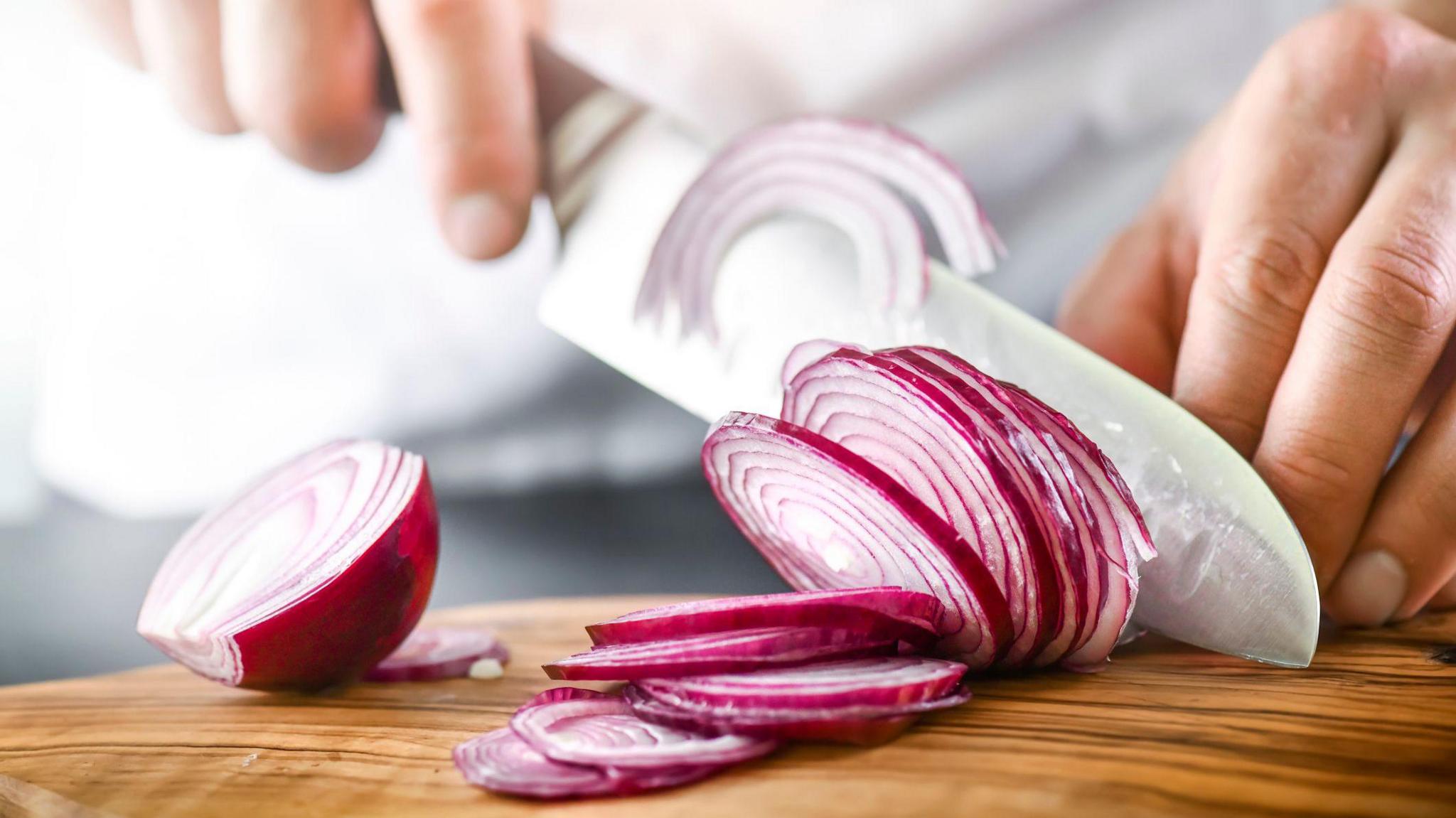 The picture shows an adult's hands chopping a red onion. 