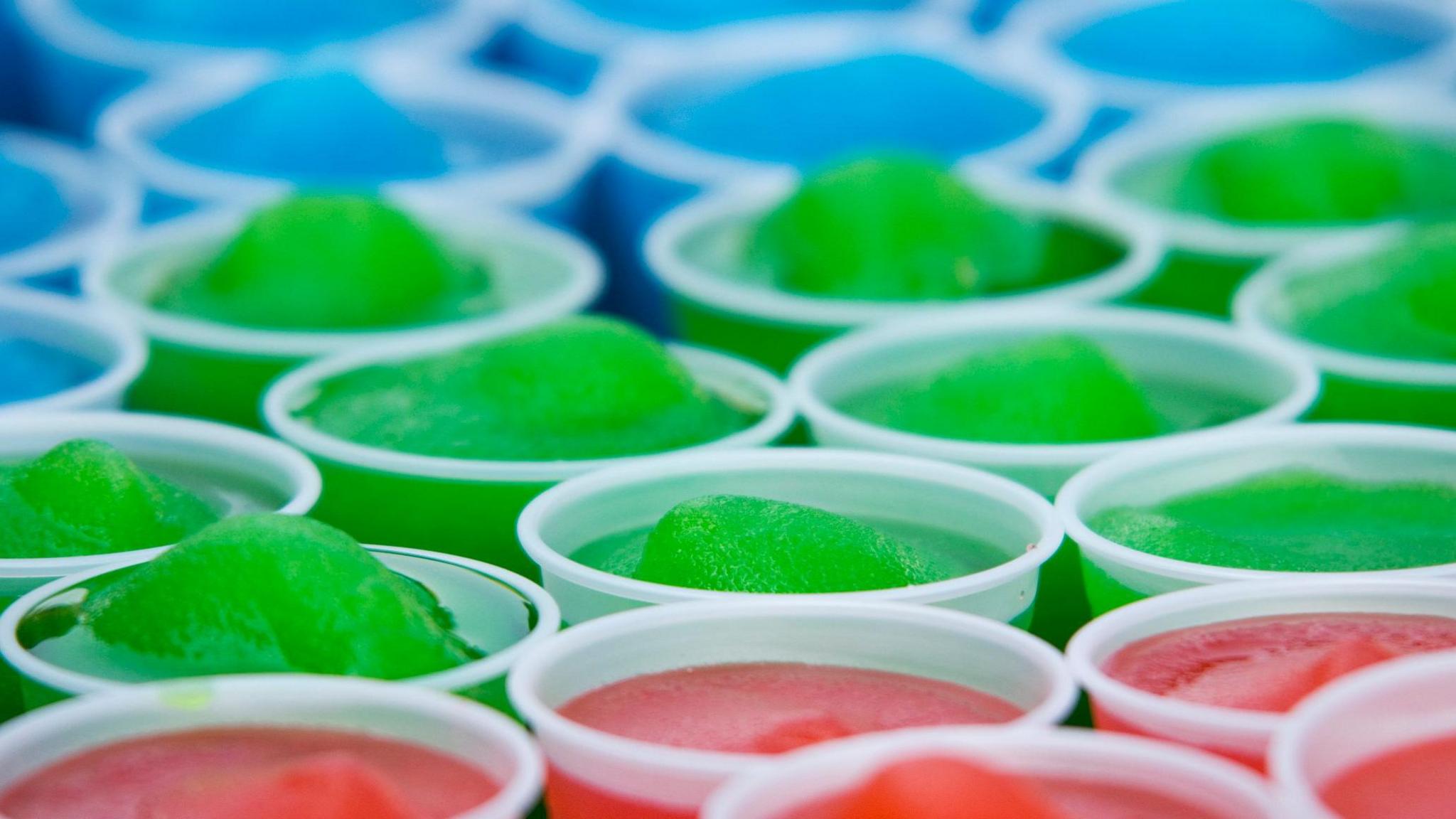 Slushy ice drinks coloured blue, green and red all lined up in white plastic cups