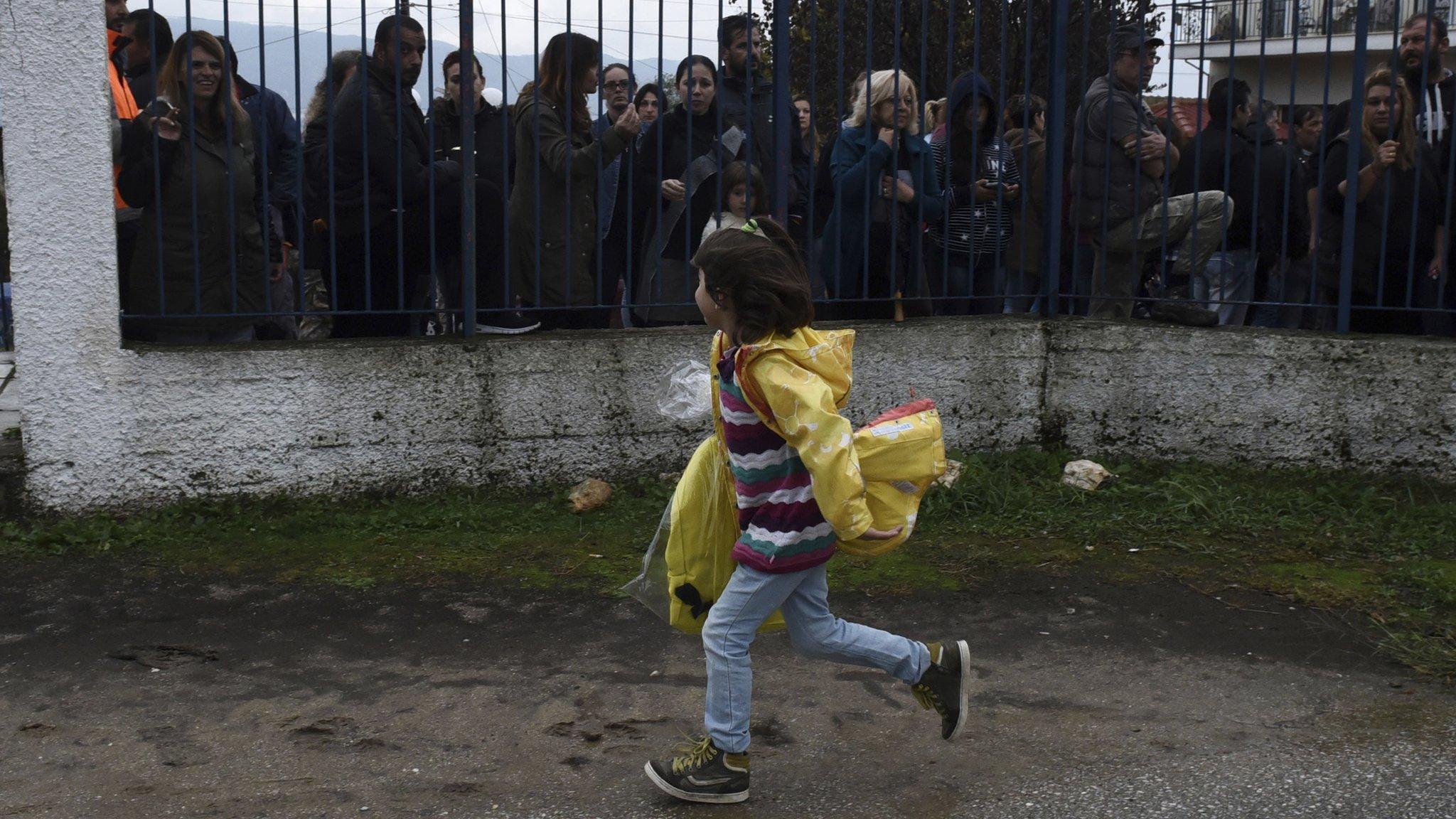 A refugee girl runs as local residents hold a protest outside a school at the Greek village of Profitis some 35 kilometers (22 miles) east of Thessaloniki, on Monday, Oct. 10, 2016.