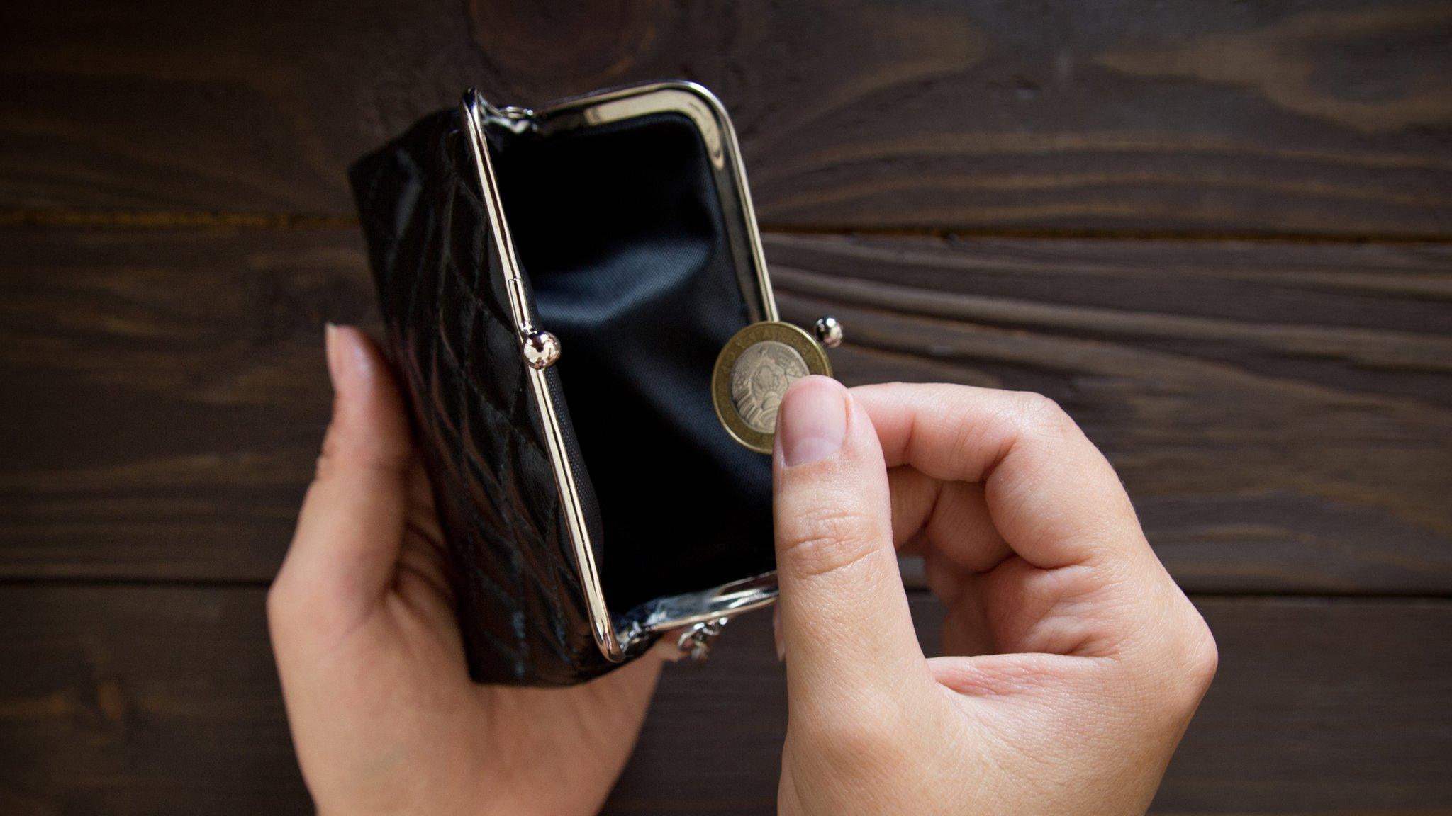 A hand pulling out a £1 coin out of a black purse