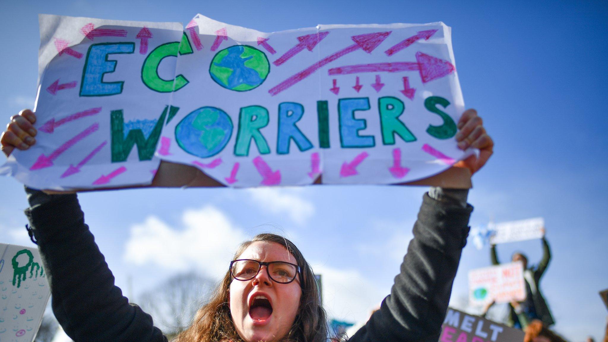 a girl holds up a sign that reads eco worriers at a protest