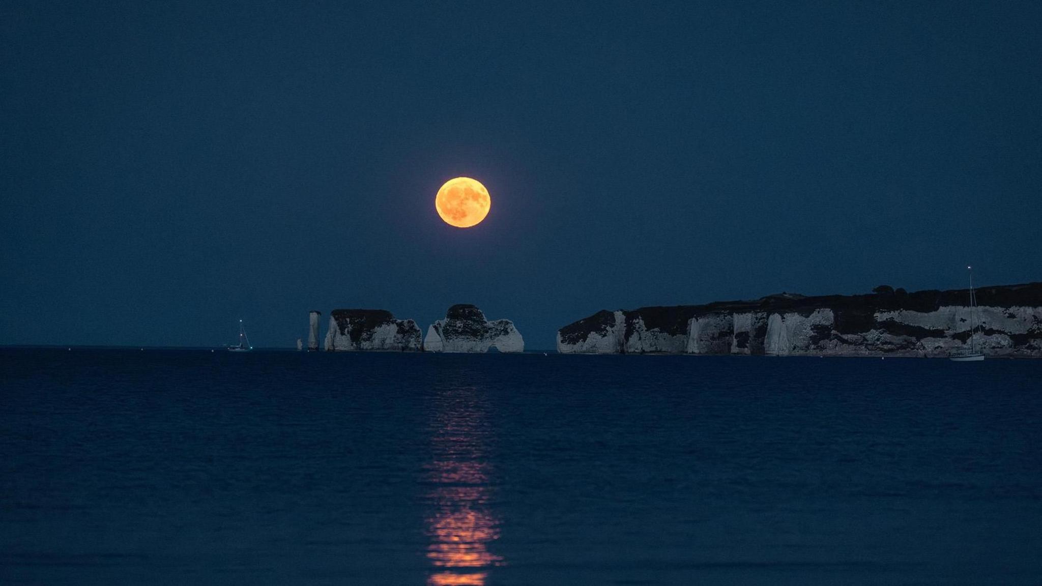 Another shot of the same rock formation from further back. The moon is higher in the sky, casting an orange reflection across the sea.