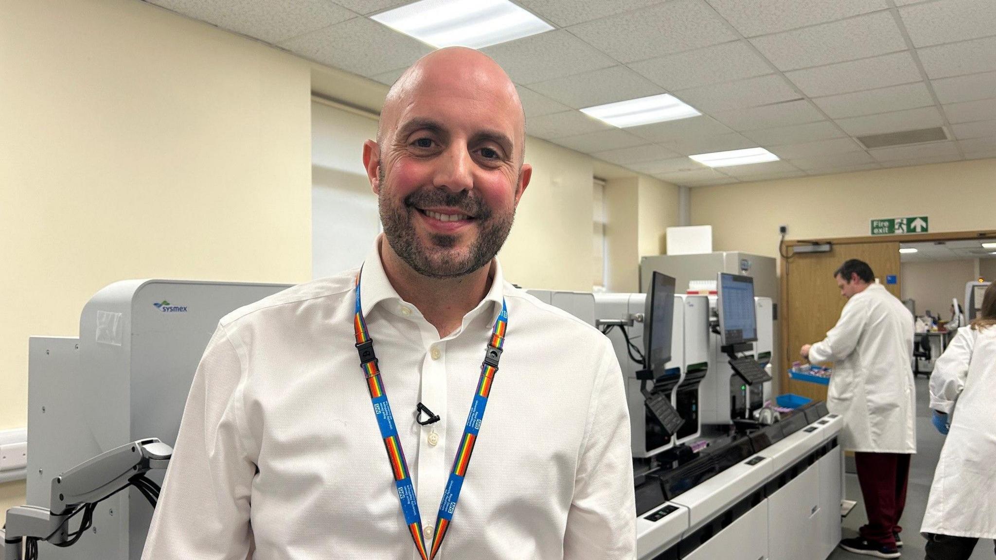 A man smiling whilst standing in a medical lab.