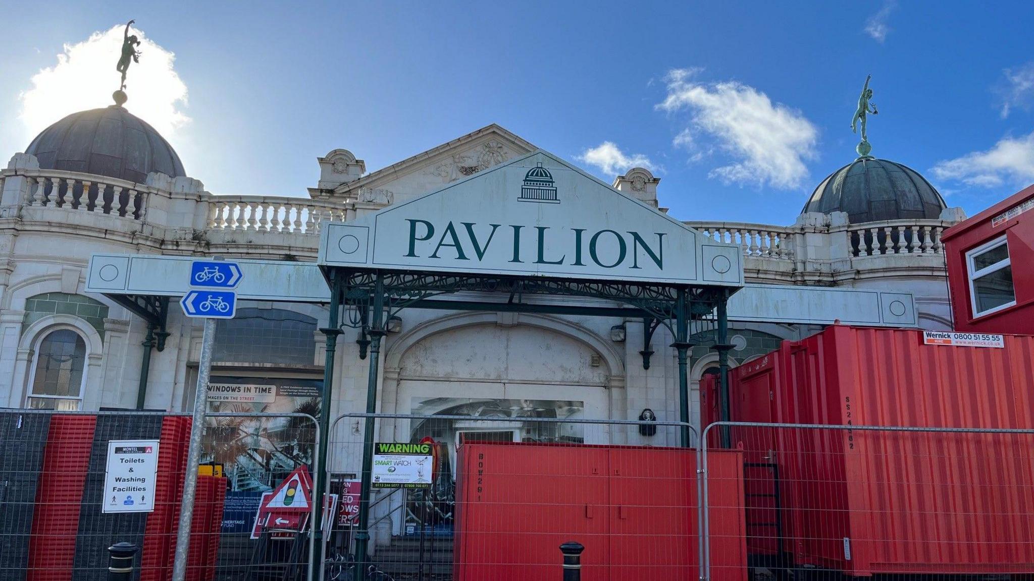 The front of the derelict Torquay Pavilion site with red containers and fencing in front of the building