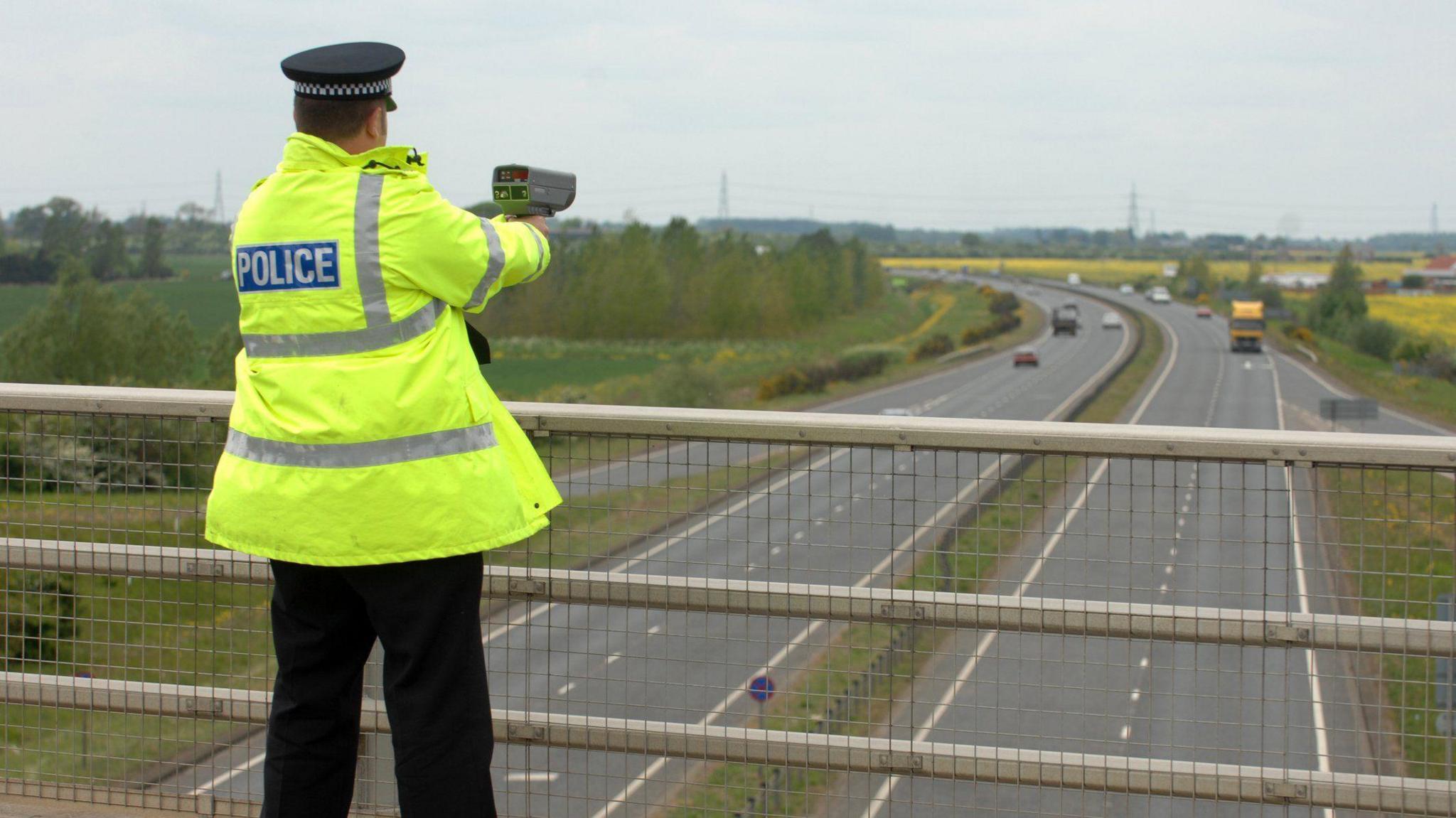 A police officer conducts a speed camera check over a dual carriageway