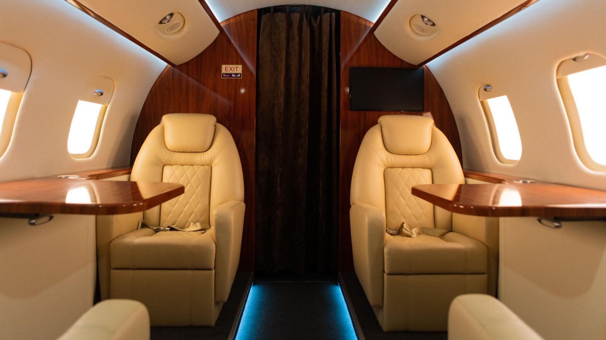 Inside a private jet with one chair and table on each side of the aisle