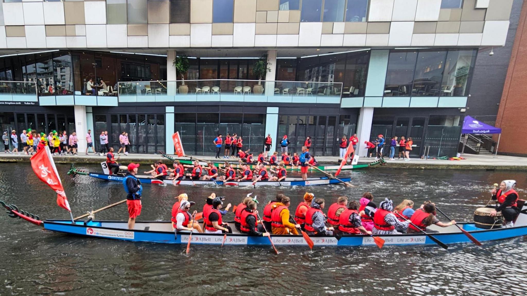 rowers in red life jackets on boats in the canal