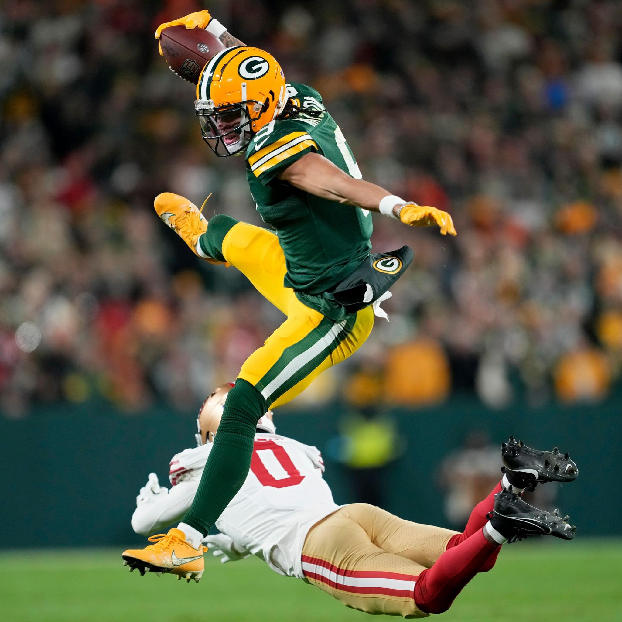 Christian Watson of the Green Bay Packers leaps over Renardo Green of the San Francisco 49ers while running with the ball in the third quarter at Lambeau Field on 24 November 2024 in Green Bay, Wisconsin.