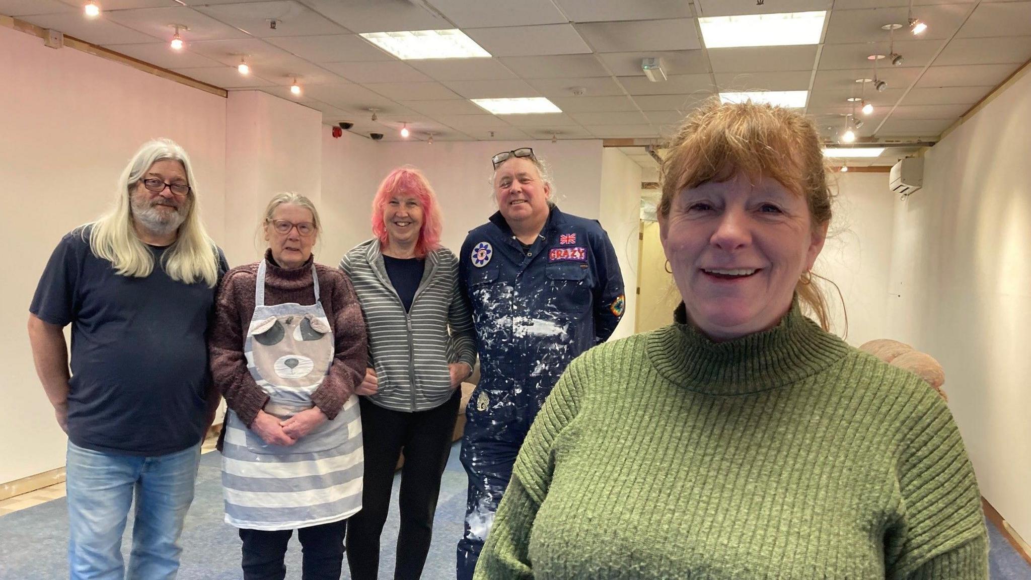 Five people lined up inside a gallery space with freshly painted white walls. 