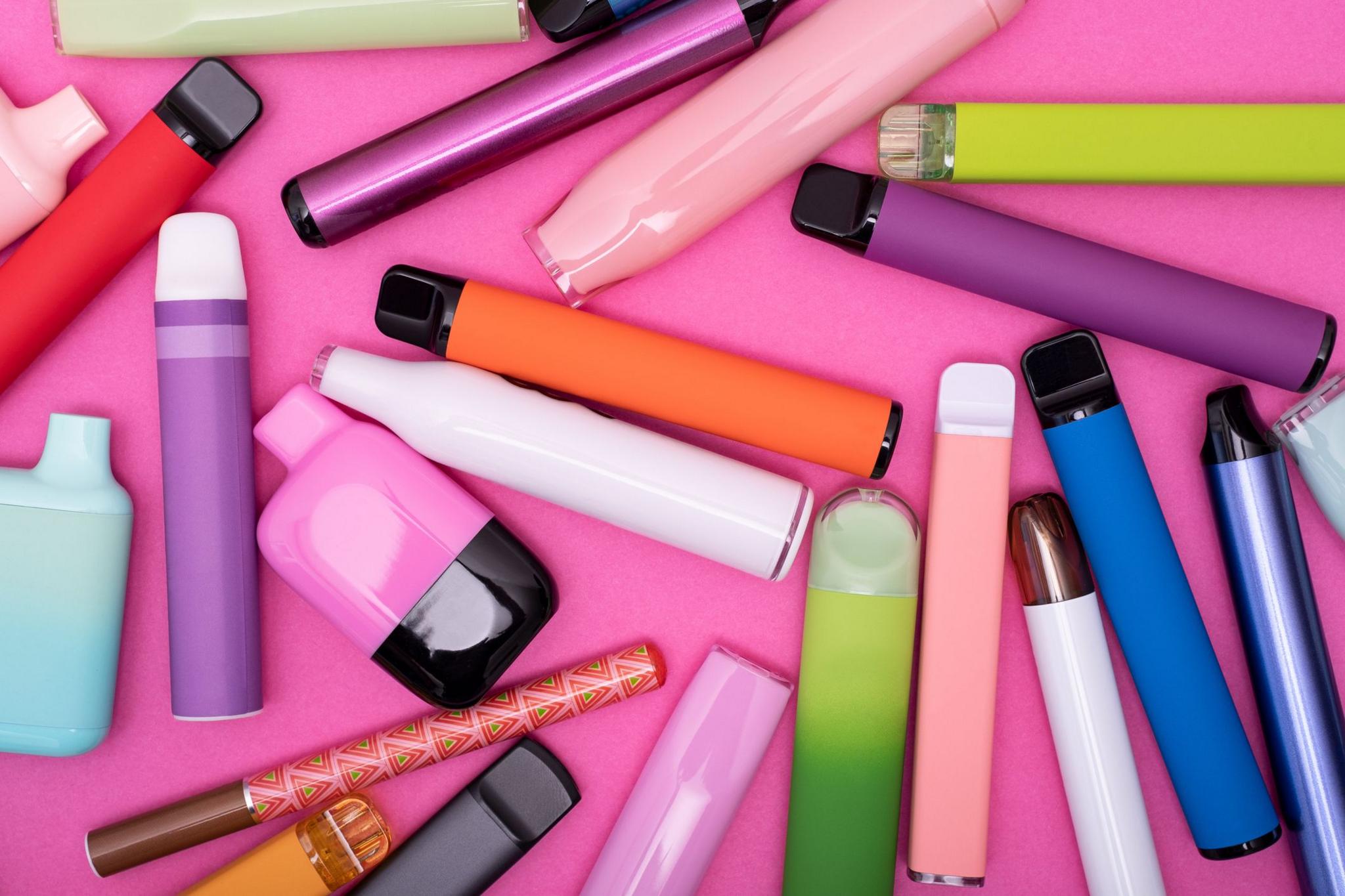 Various colourful disposable vapes on a bright pink background