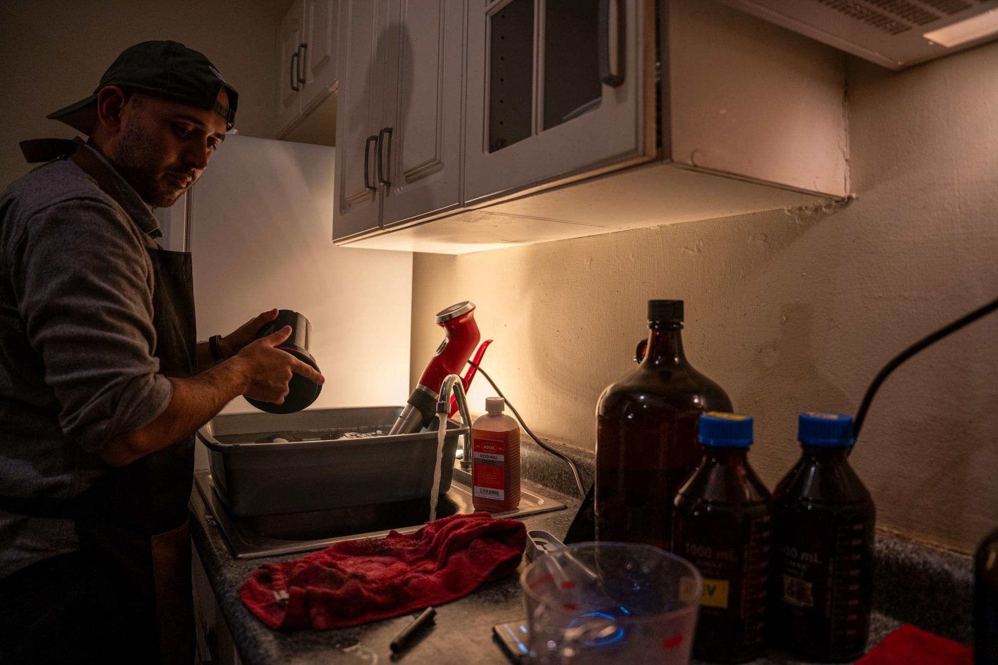 Fabriccio Díaz, wearing a back-to-frong baseball cap, is moving the container with the developing film around for the chemicals to mix evenly with the film roll.