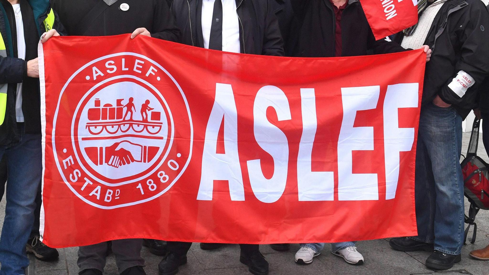 A close up shot of five people holding up a red rectangular banner reading: Aslef with an Aslef logo on the left.