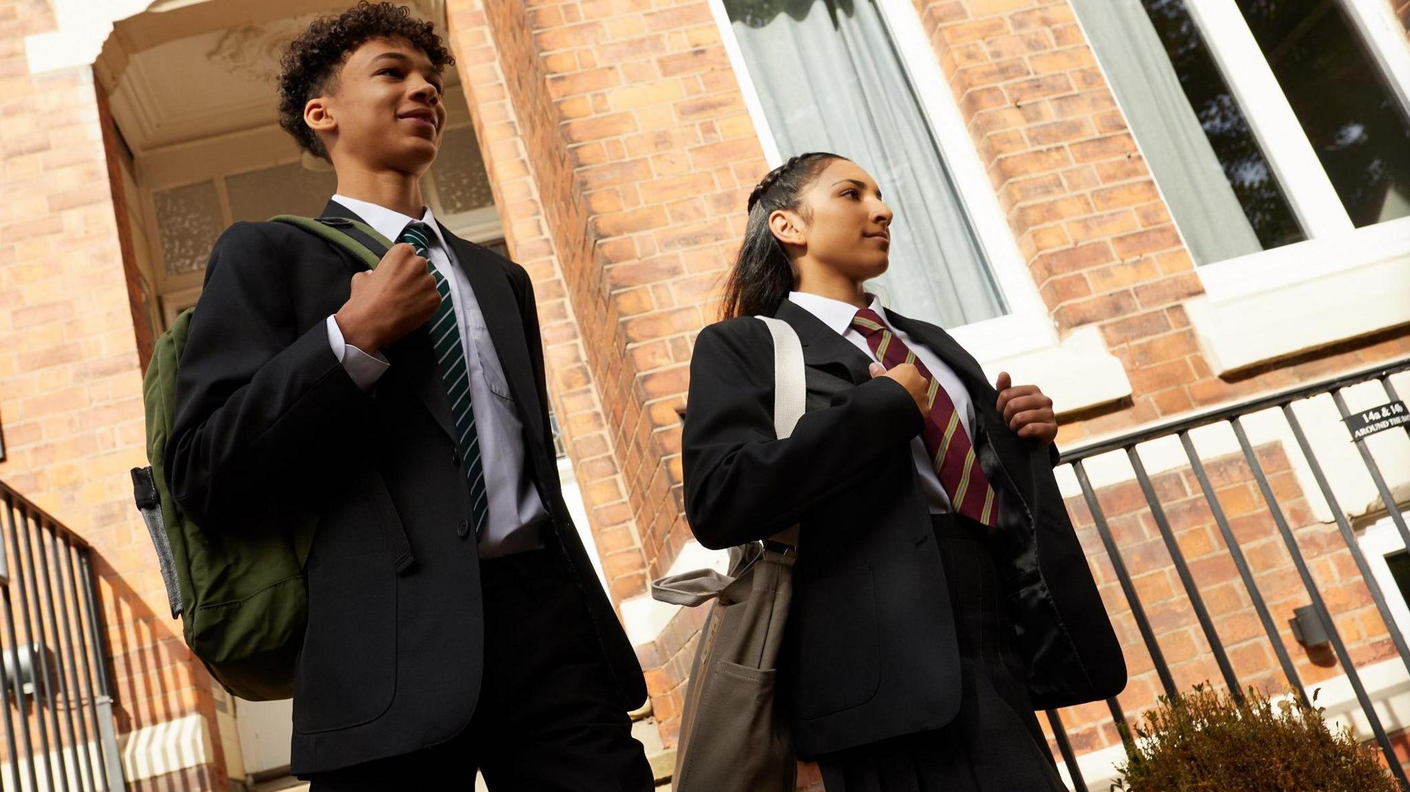 Two school children wearing blazers and ties leaving the house.