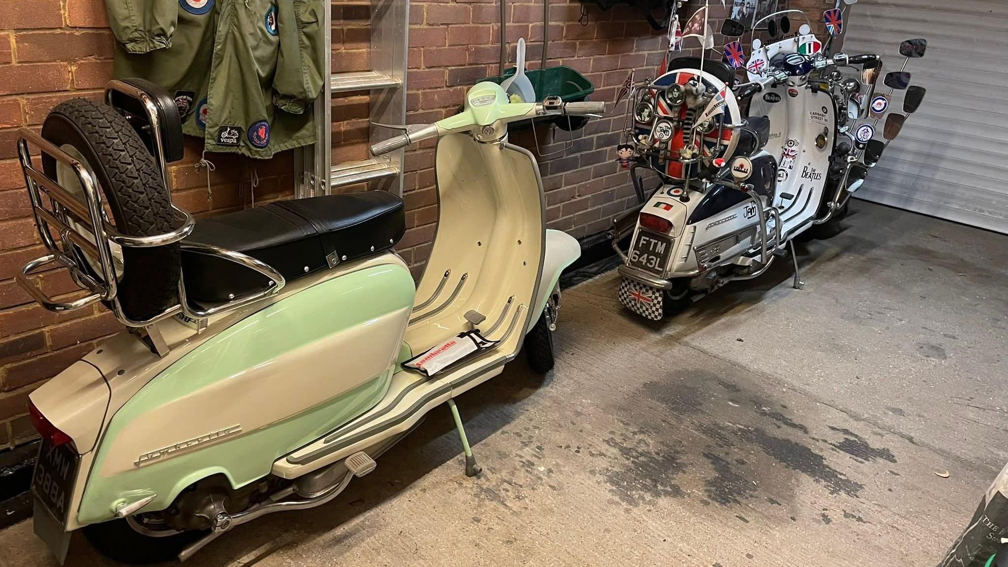 A cream 1963 Lambretta, with cyan markings, parked inside a garage. It is stationed next to another vintage bike.