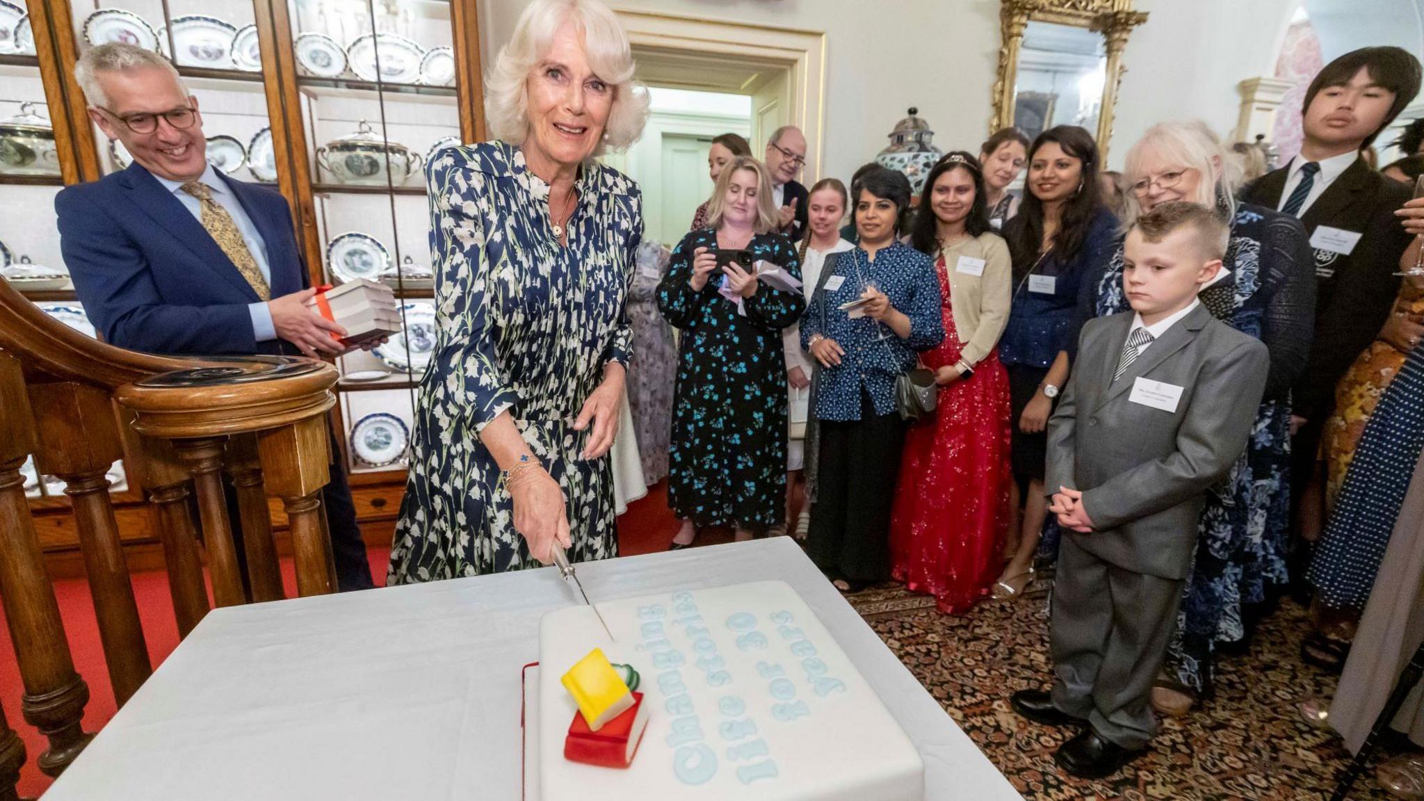 Queen cutting the cake while everyone looks on