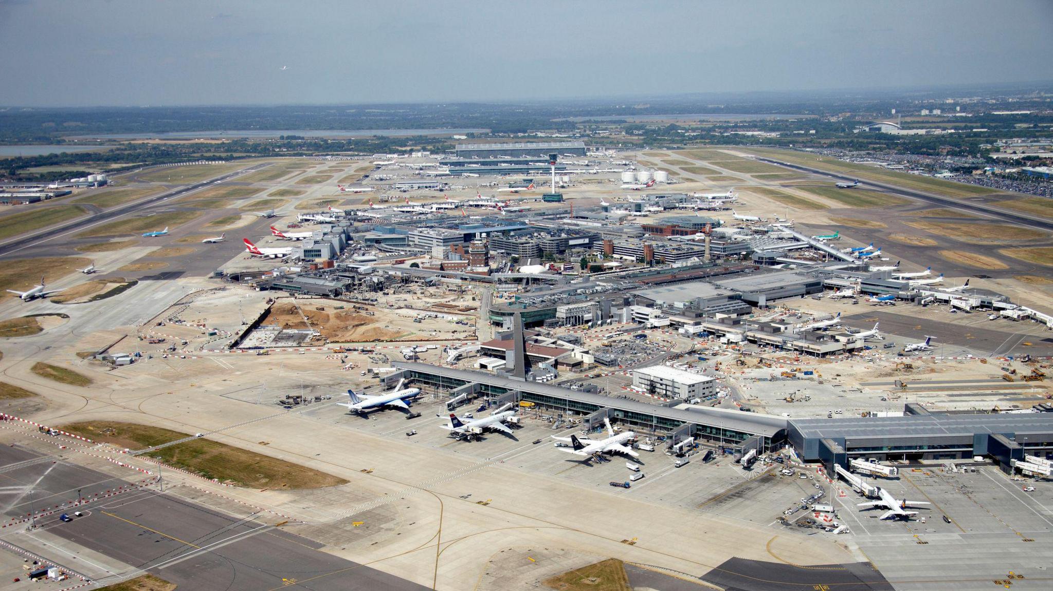 An aerial view of Heathrow Airport, showcasing multiple terminals, runways, and parked airplanes. 