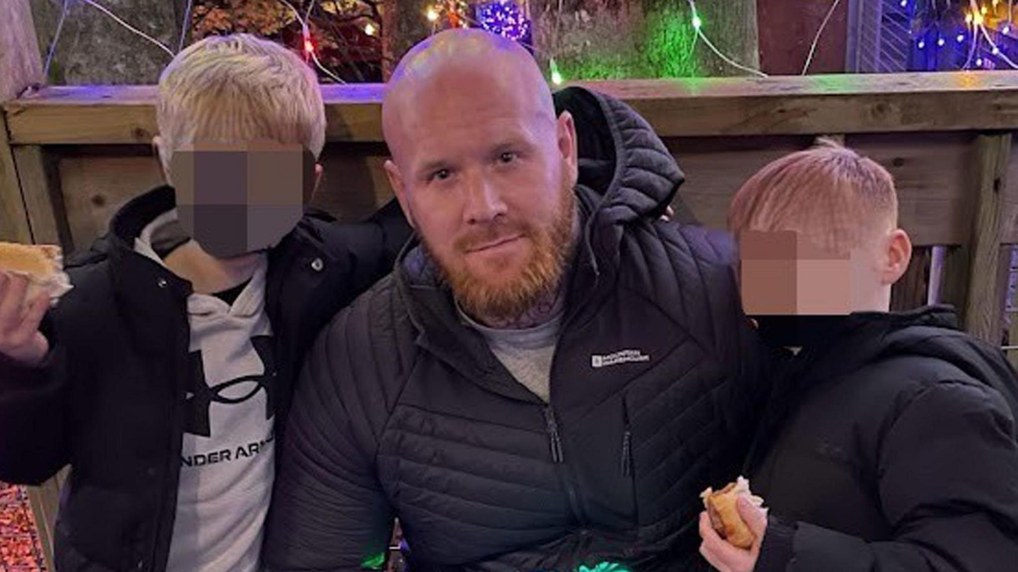 A police handout of Lenny Scott with two of his children. He is crouching down with his arms around them. The boys' faces have been blurred.