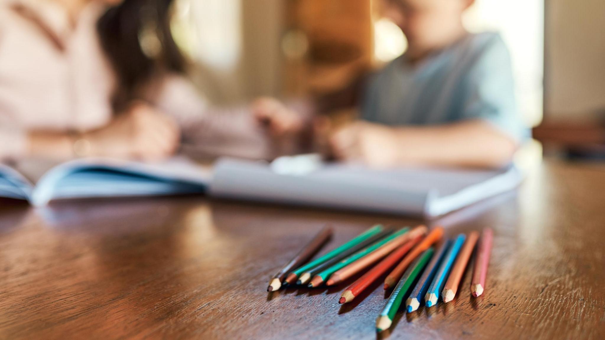 Child doing an activity with an adult including colouring pencils