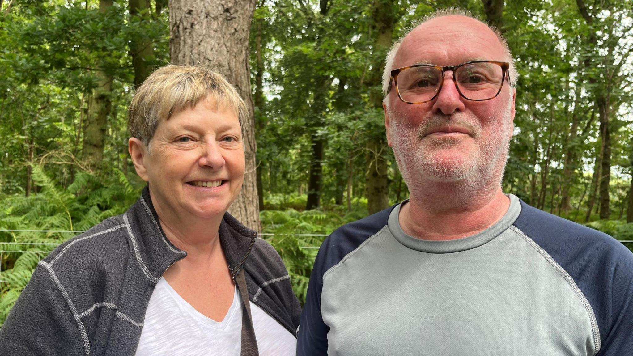 Alan and Denise Hall smiling at the camera while standing in the woods.