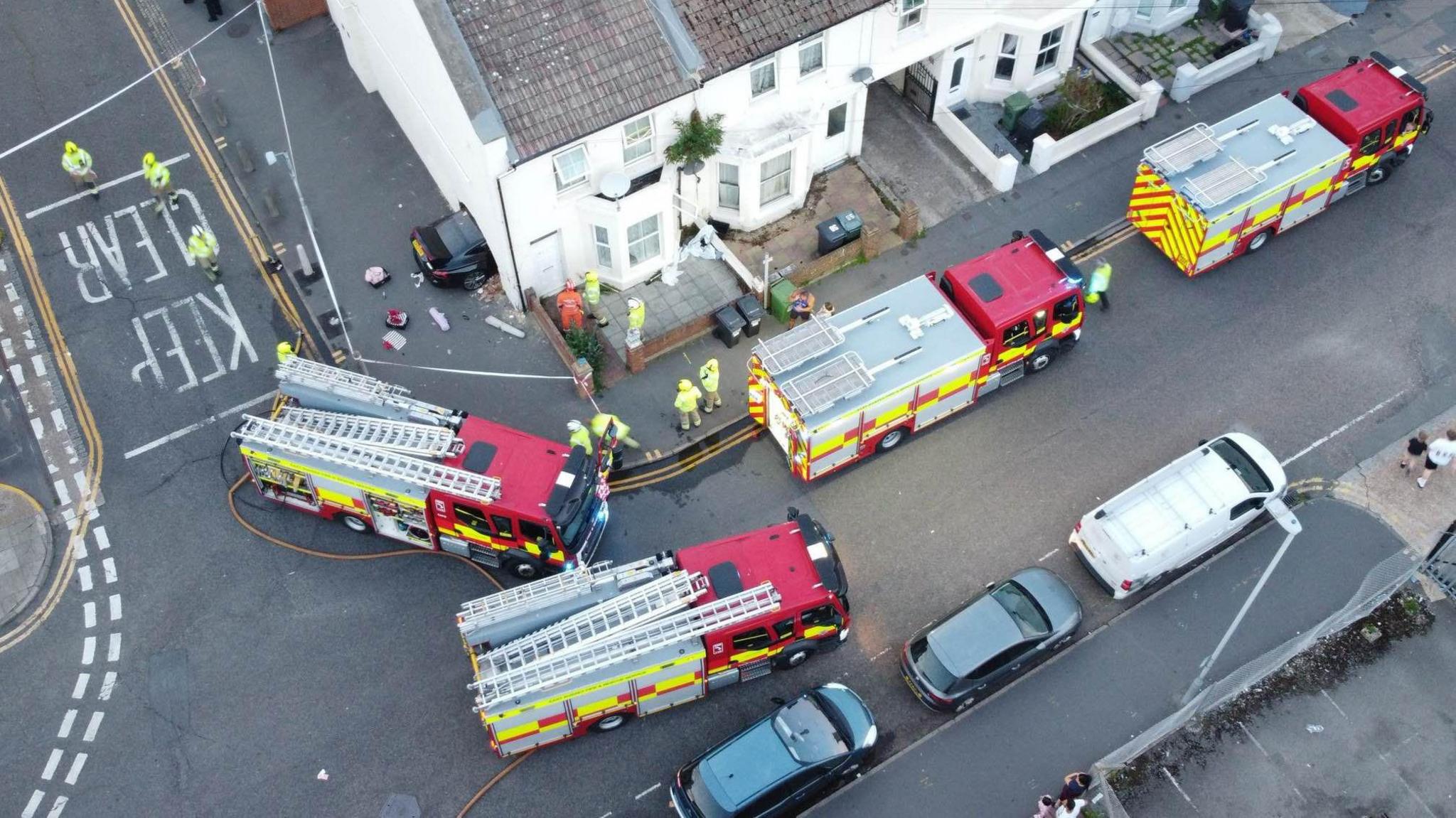 Four fire engines surround a house with a car seen halfway through the exterior wall of the property. 