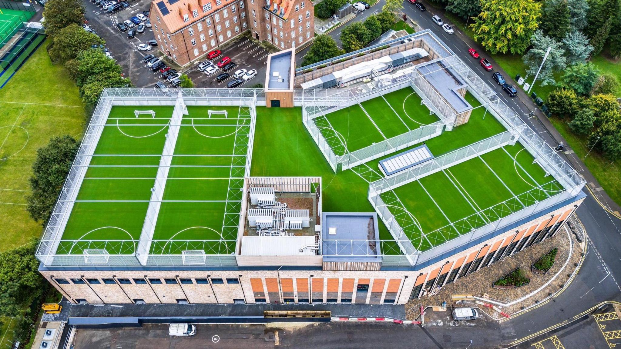 An aerial image of four green multi-sport rooftop pitches.