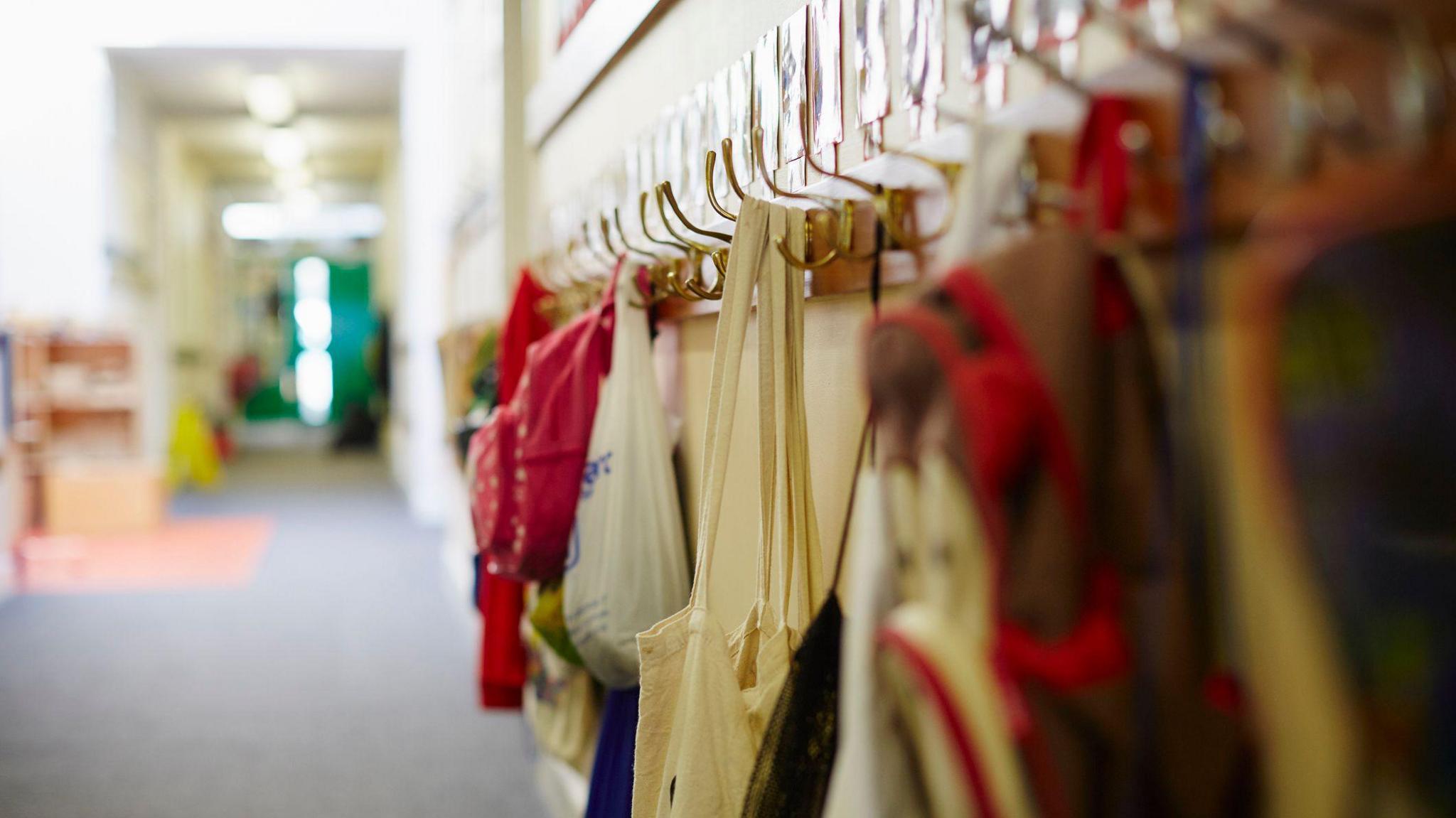 A generic picture of a primary school, with schoolbags hung up on pegs on a wall.