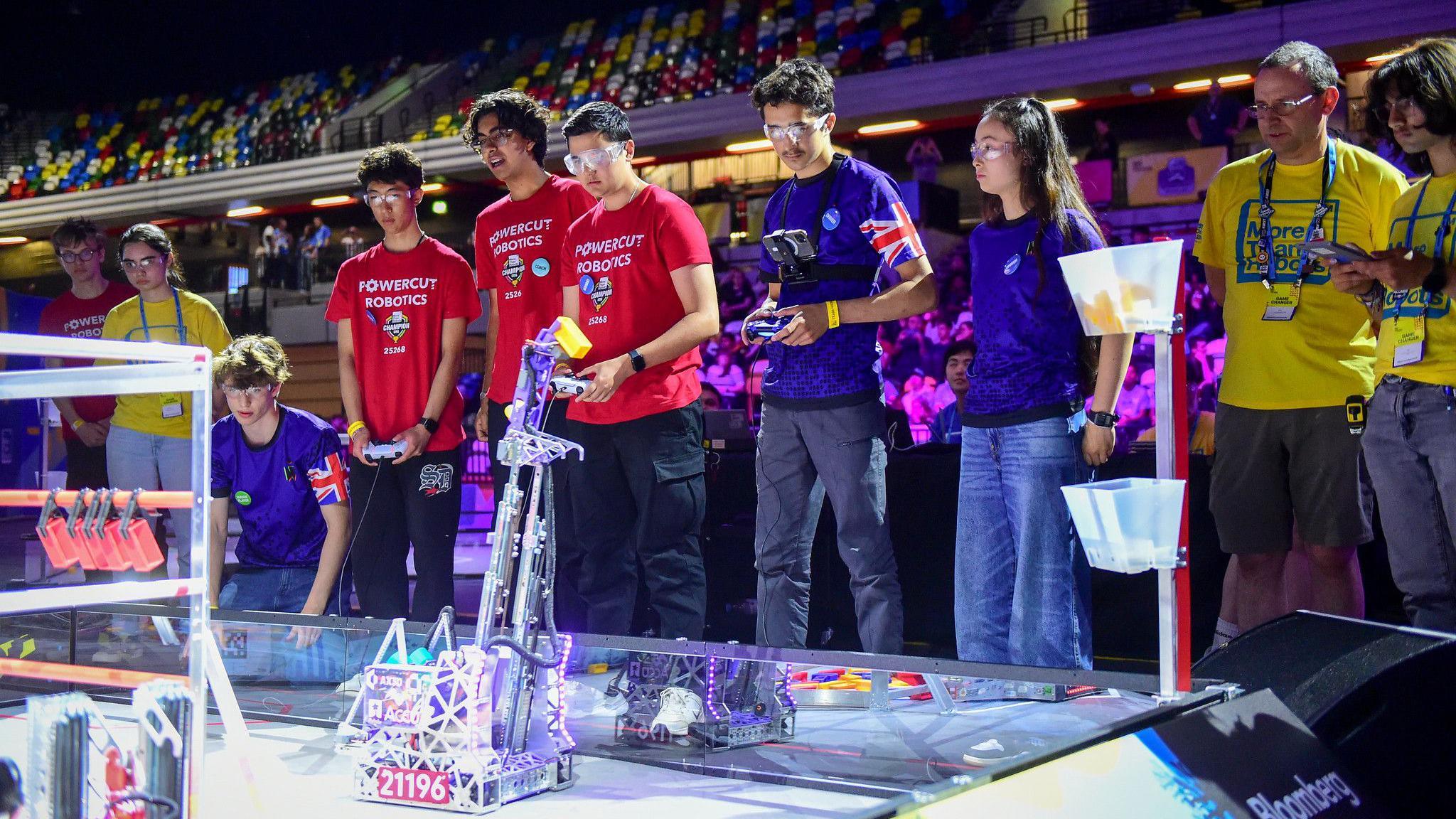 A group of students with remote controls watch on as they compete with their robots.
