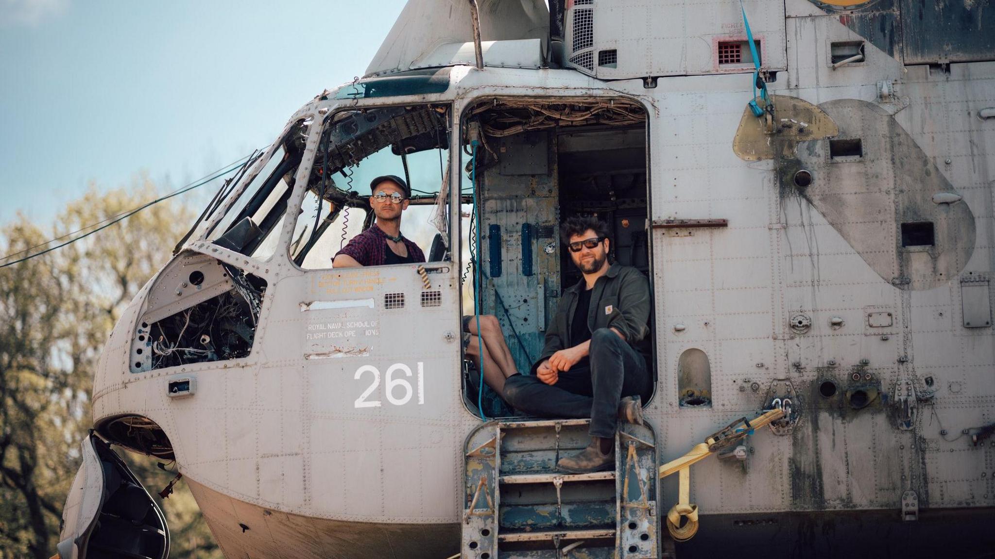 Two men sitting in the old helicopter which will be used at Arcadia at Glastonbury