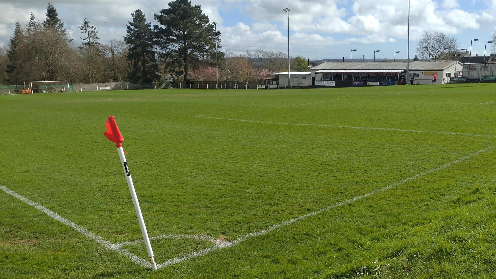 A football pitch with a red corner flag and single story pavilion on one side