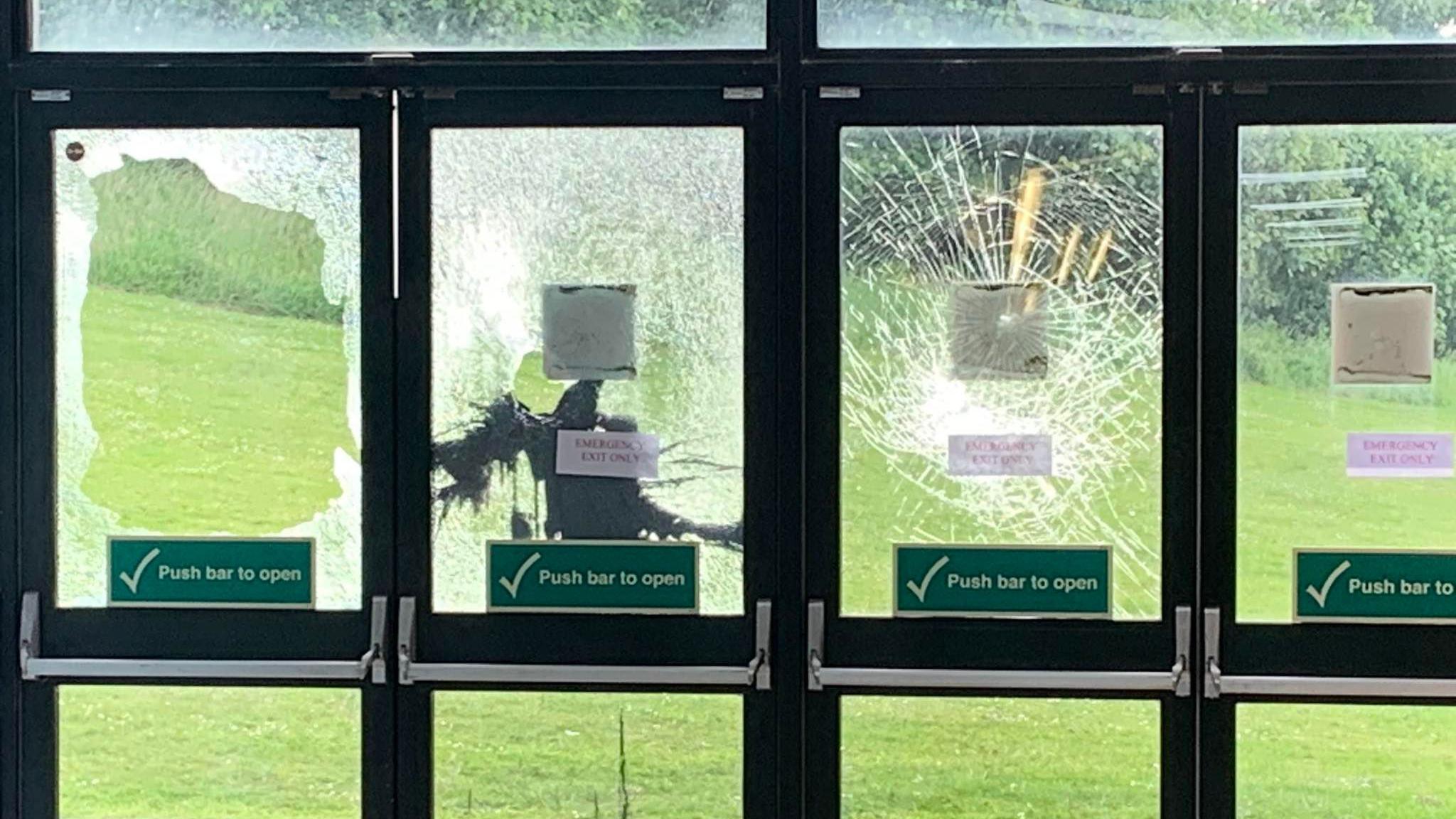 Fire exit doors with smashed glass. The doors are black and there a green 'push bar to open' stickers on the windows.