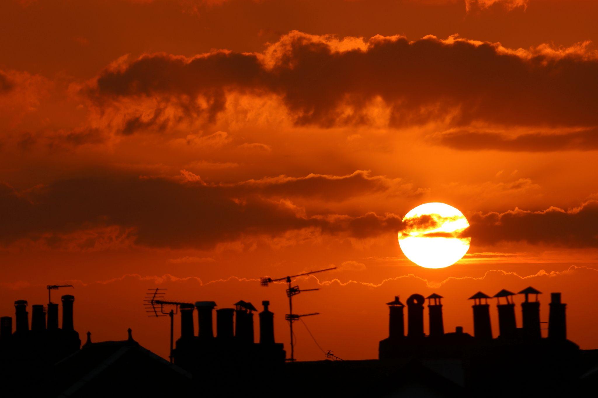 Vivid burnt orange sky with the sun setting above the silhouette of chimneys
