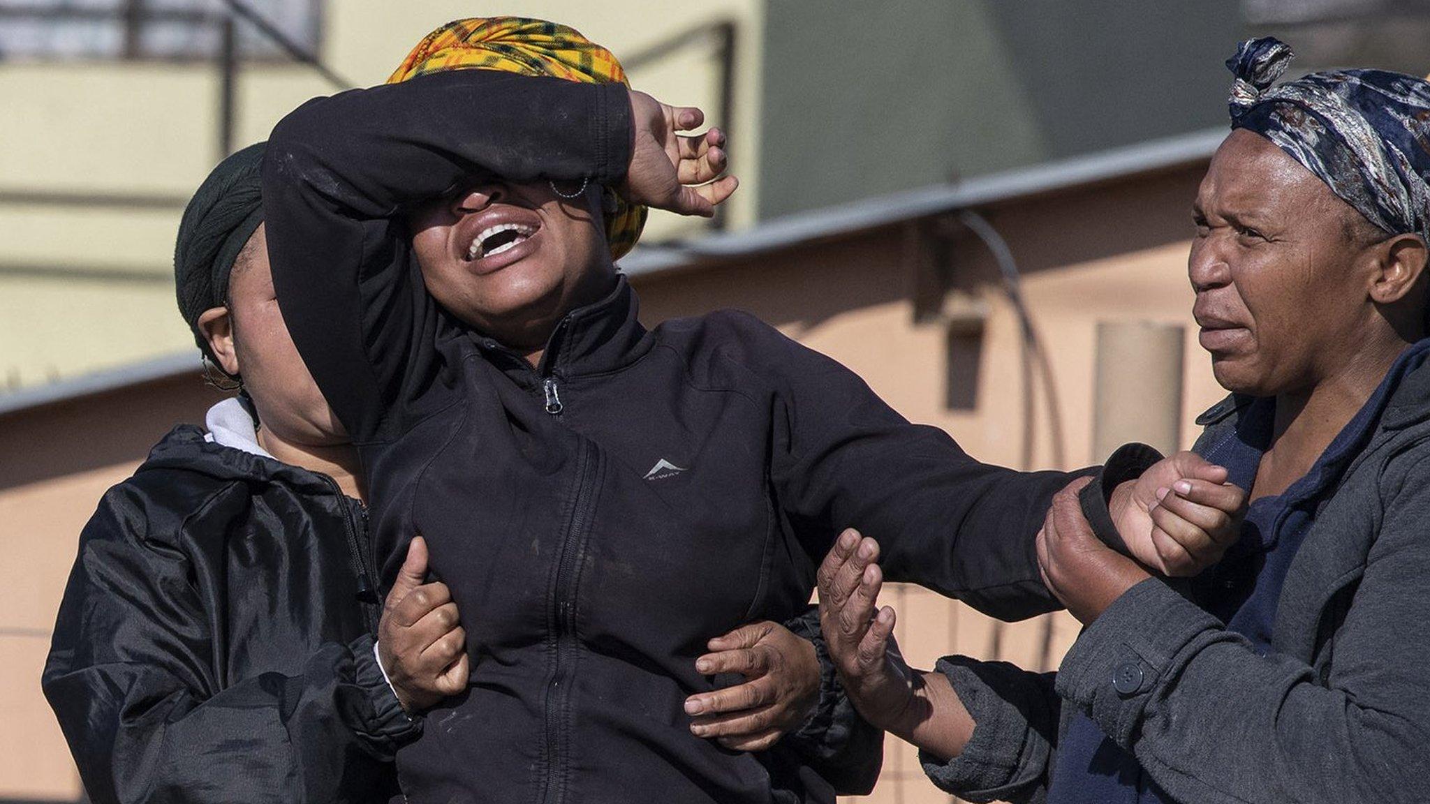 A relative of one of the victims cries as south African Police Service officers refuse to let her cross the police barrier and enter the crime scene in Soweto, South Africa, on July 10, 2022