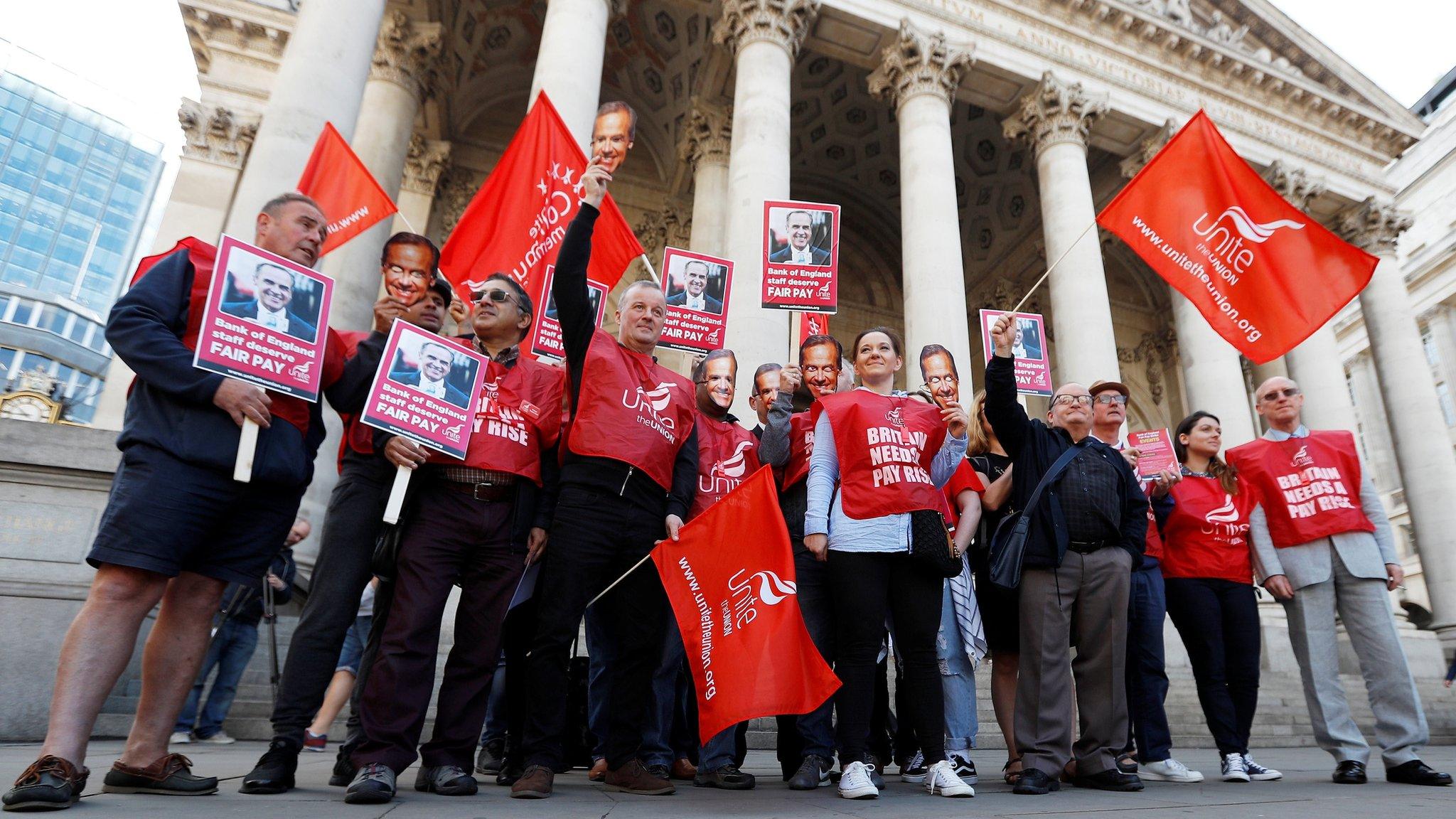 Strikers hold up Bank of England Governor Mark Carney masks and wave flags and placards outside the bank as it staff begins a three day strike over pay, in the City of London, Britain, August 1, 2017.