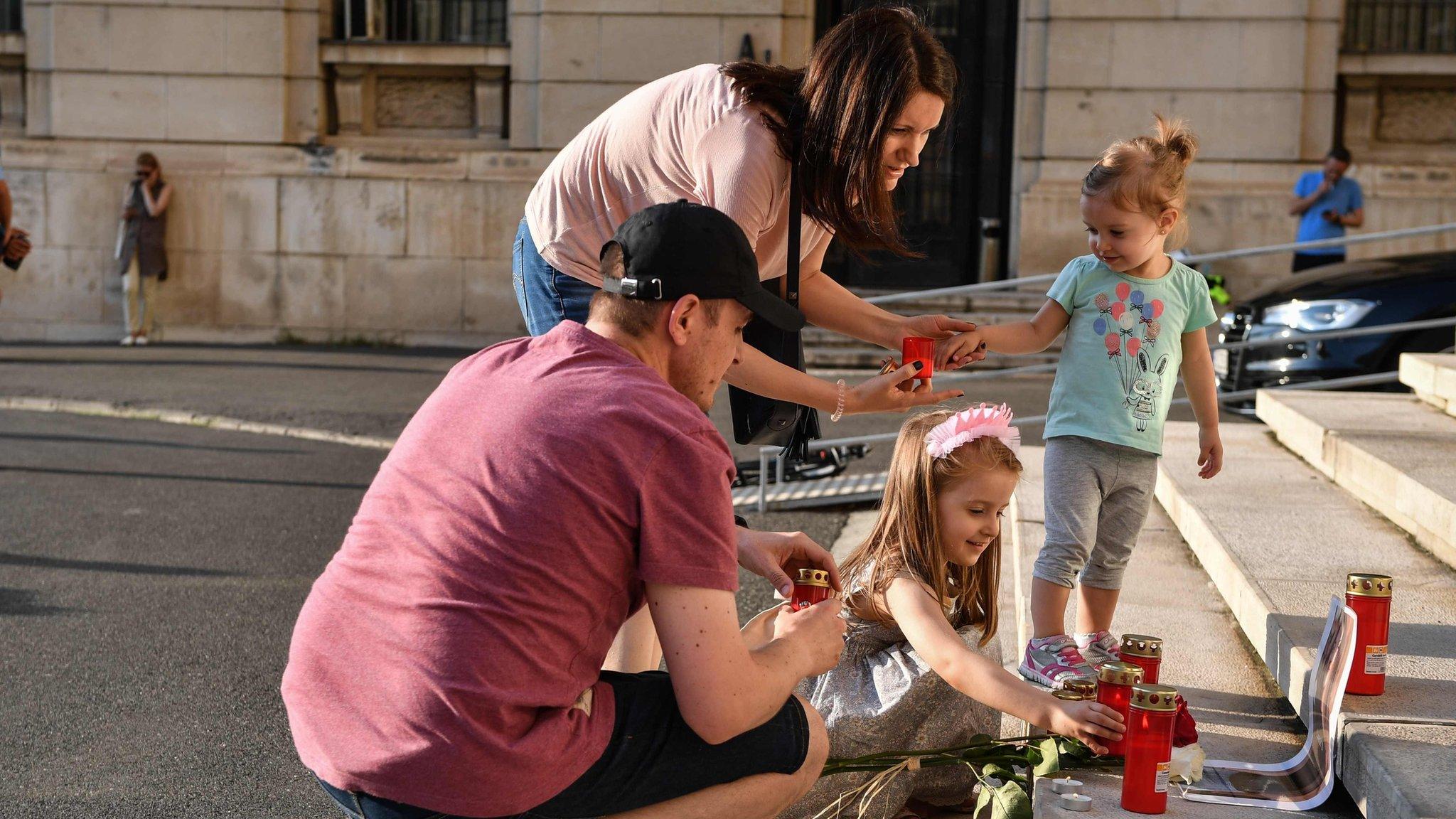 A family lights candles on the main entrance of the Romanian Ministry of Interior in Bucharest on July 27, 2019, next to the portrait on Alexandra, a 15-year-old girl who has being murdered after she telephoned three times to report her own kidnapping