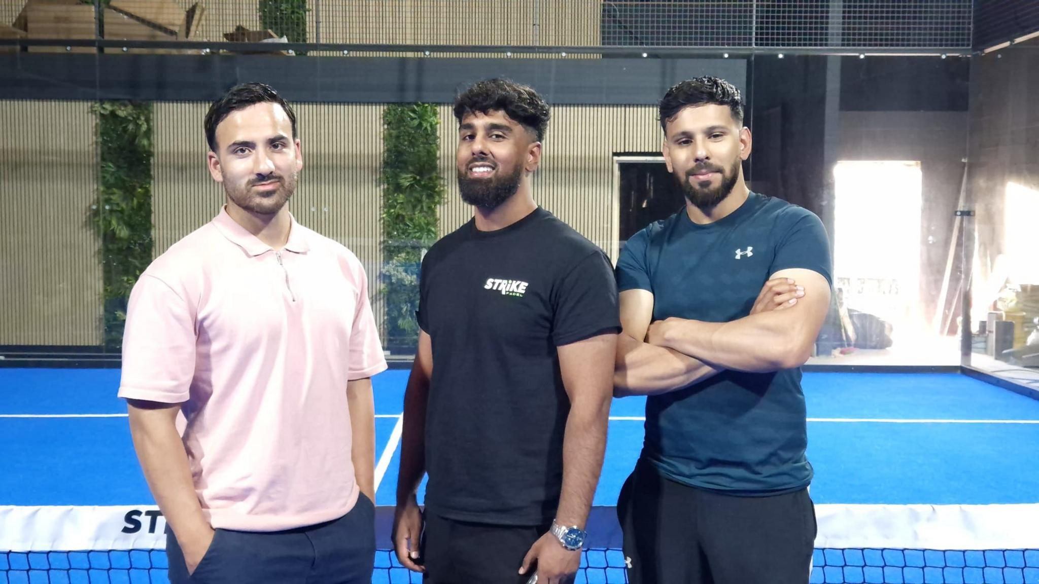 Three men standing on a padel court