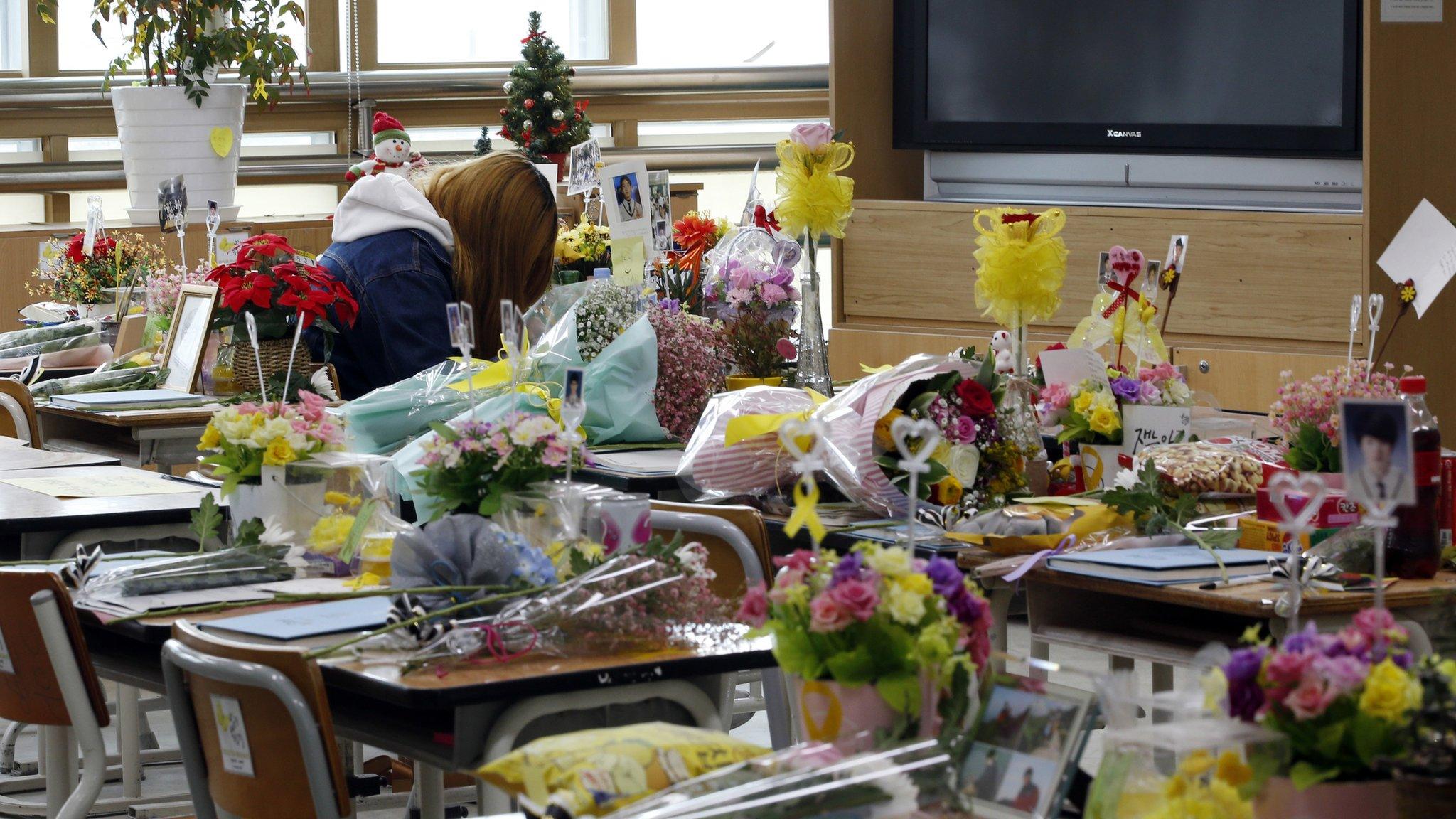 A woman leaves messages as flowers, notes and snacks from classmates and families paying tribute to the victims of the sinking of ferry Sewol are placed on the desks in a classroom, at the Danwon High School in Ansan, South Korea, Saturday, April 16, 2016.