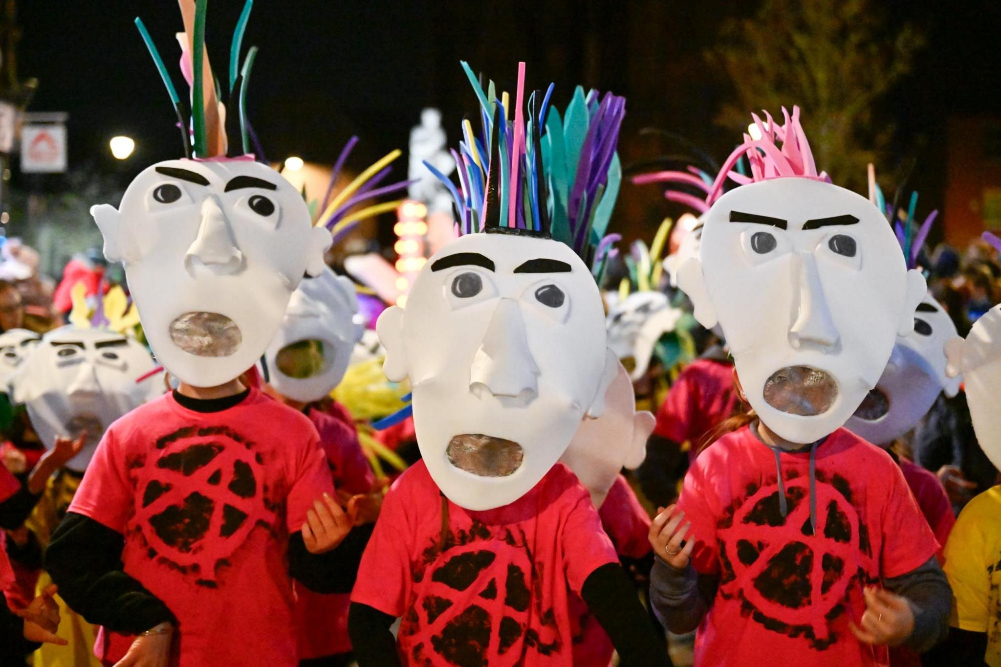 Three people in red T-shirts with white masked faces and spiky coloured paper for hair