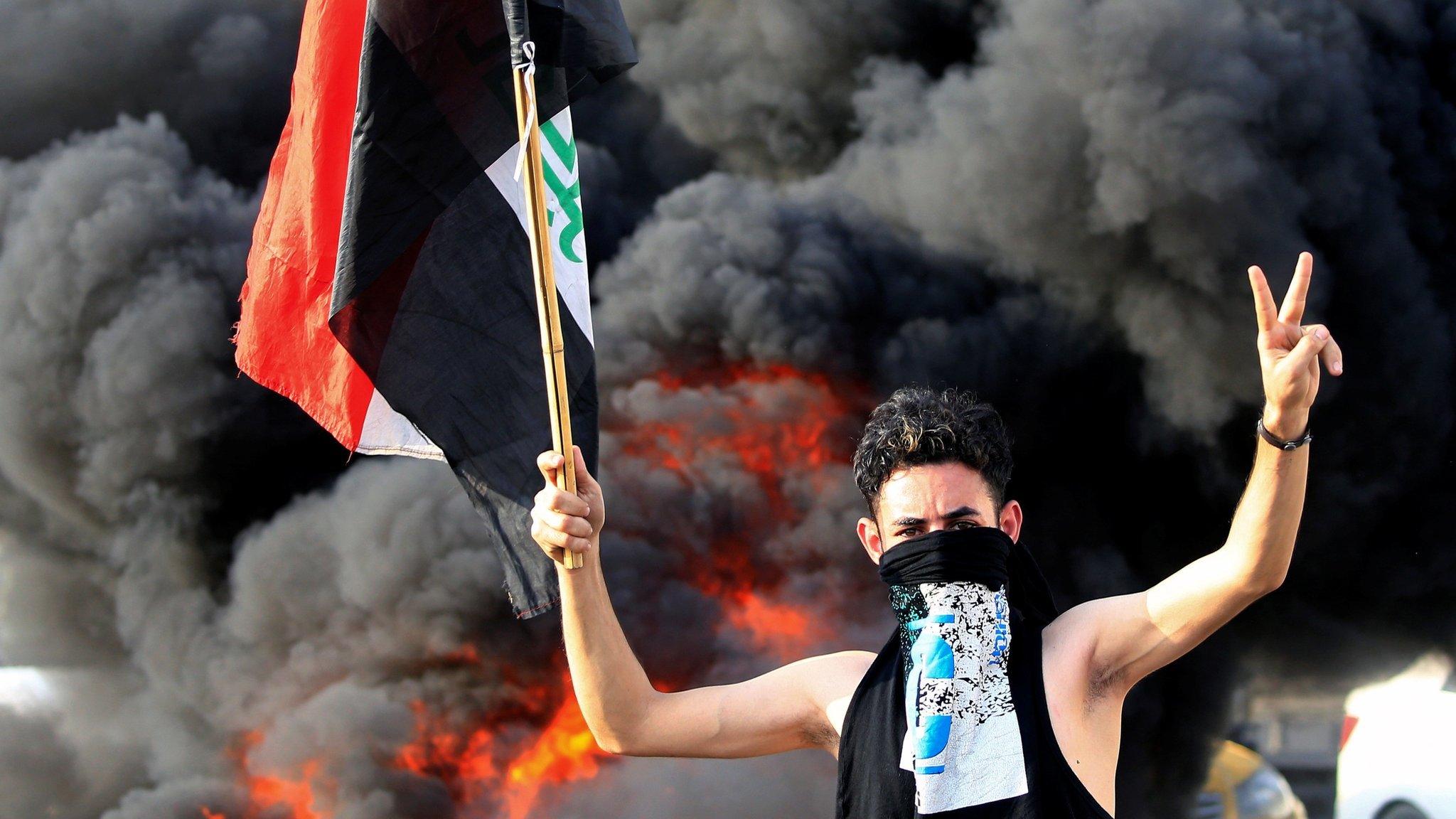 A protester gestures as he stands close to burning tyres in Baghdad, Iraq (2 October 2019)