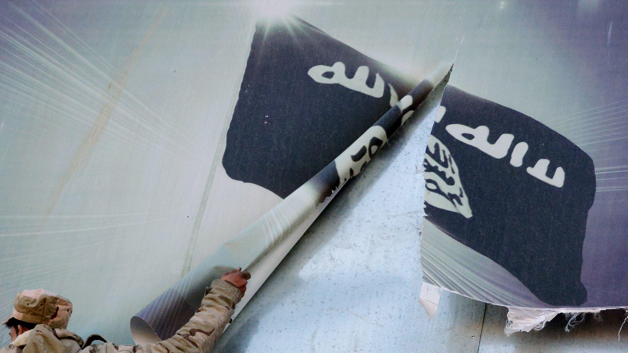 A member of the Iraqi security forces removes a banner bearing the logo of the Islamic State (IS) group in eastern Mosul on 19 January 2017