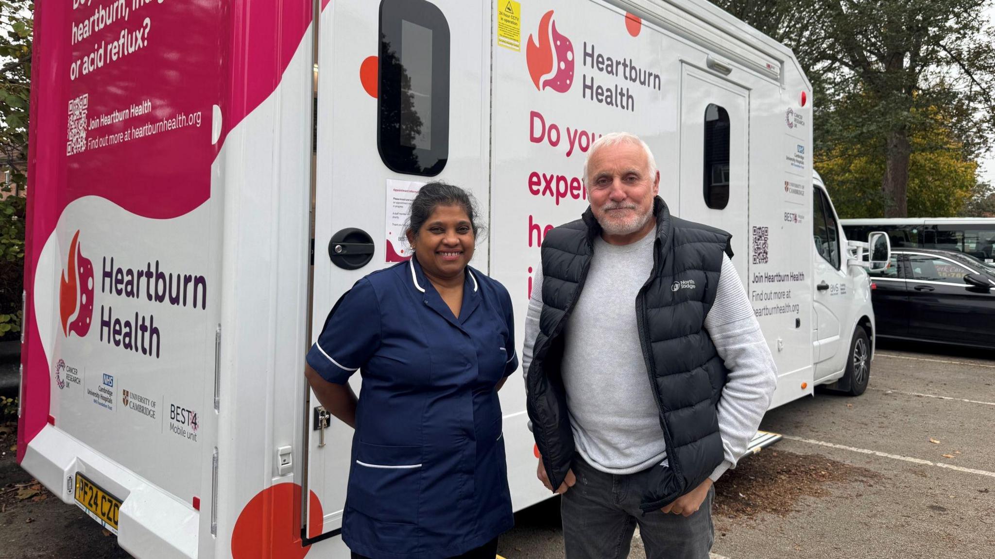 A nurse and a male patient stand in front of a mobile screening van, which has logos reading "Heartburn Health".