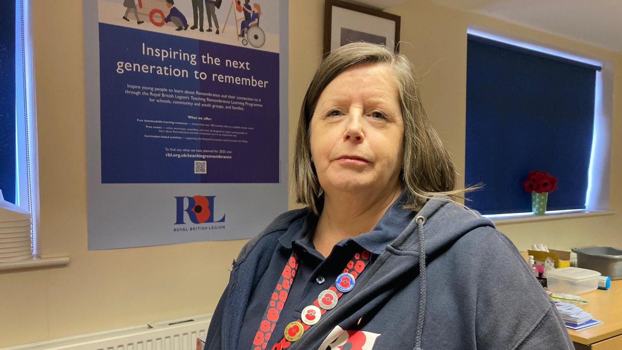 A woman wearing blue hooded top and a lanyard with a red poppy design