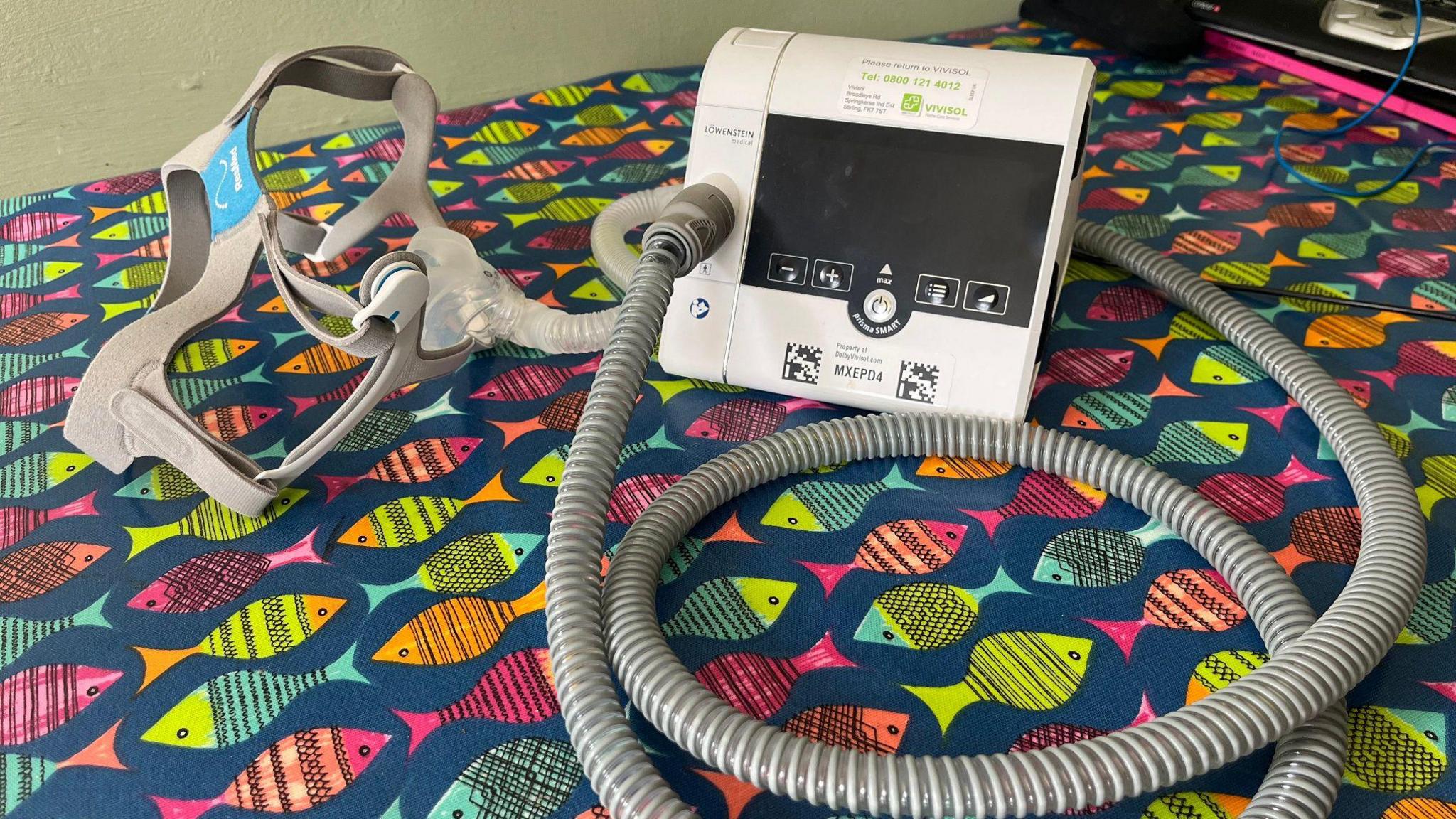 A CPAP machine - a small electronic device with a long tube coming out of it and a face mask.