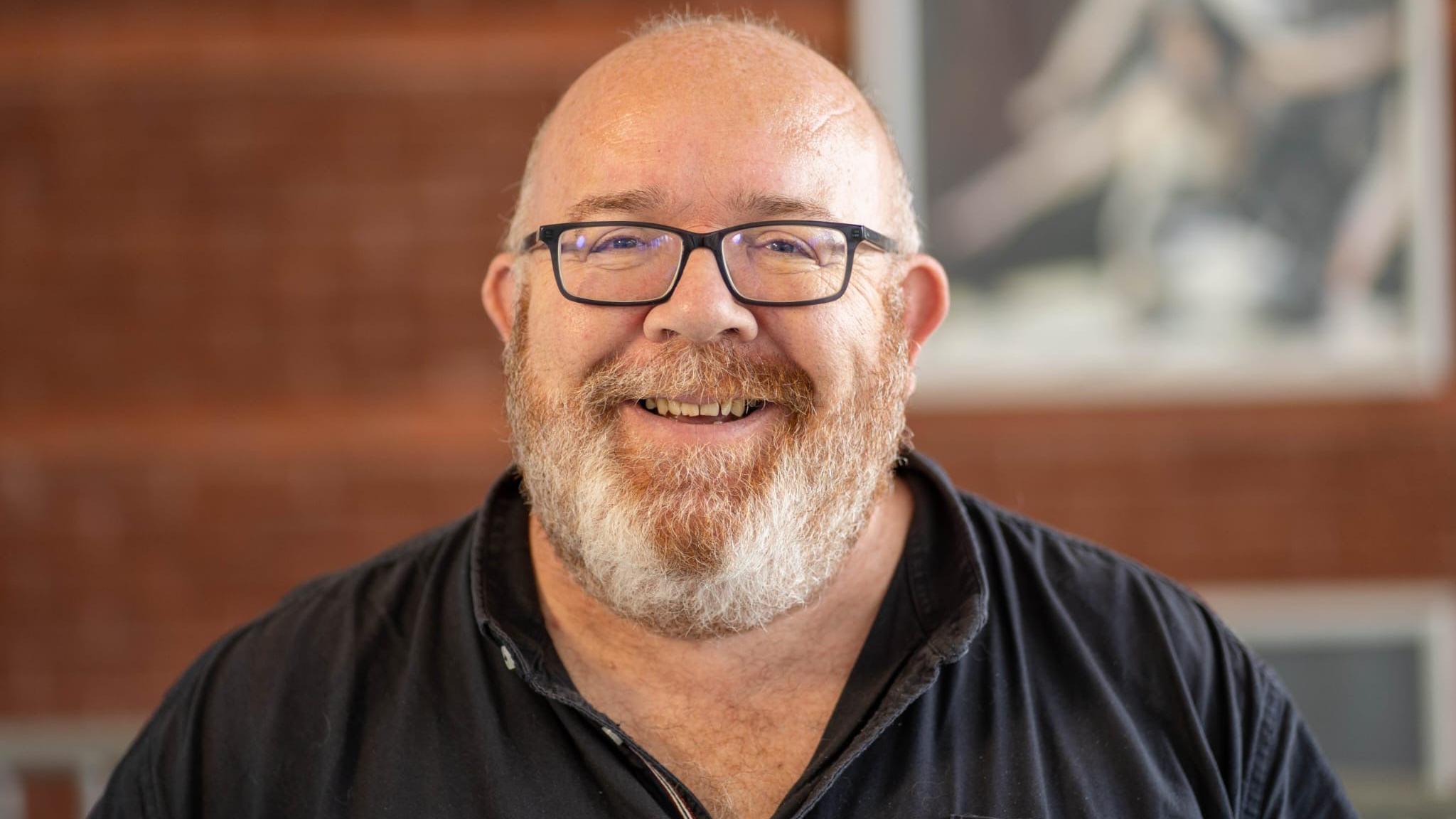 Llun o Jamie Medhurst yn gwenu wrth edrych ar y camera. Mae'n gwisgo sbectol ac mae ganddo barf gwyn.