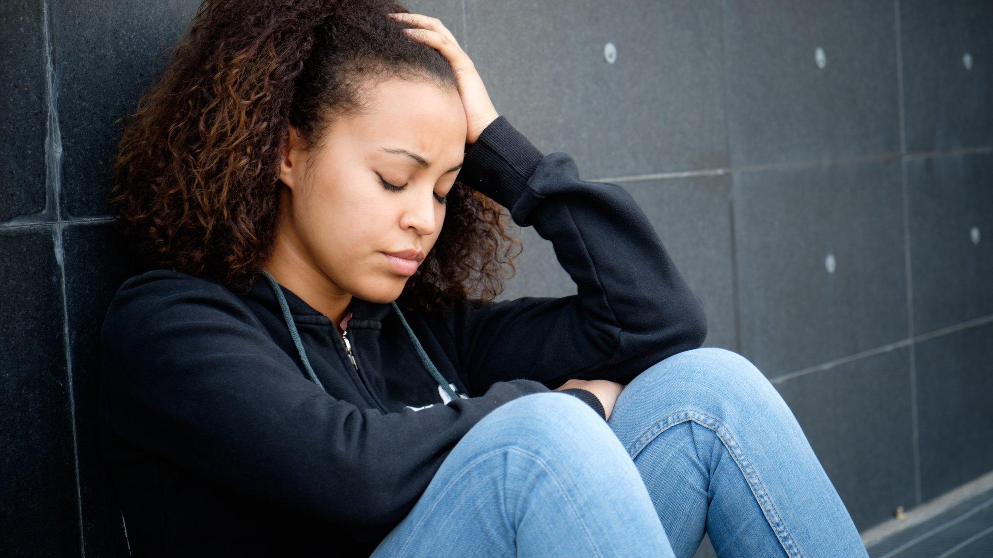 girl-sat-alone-against-a-wall-looking-sad