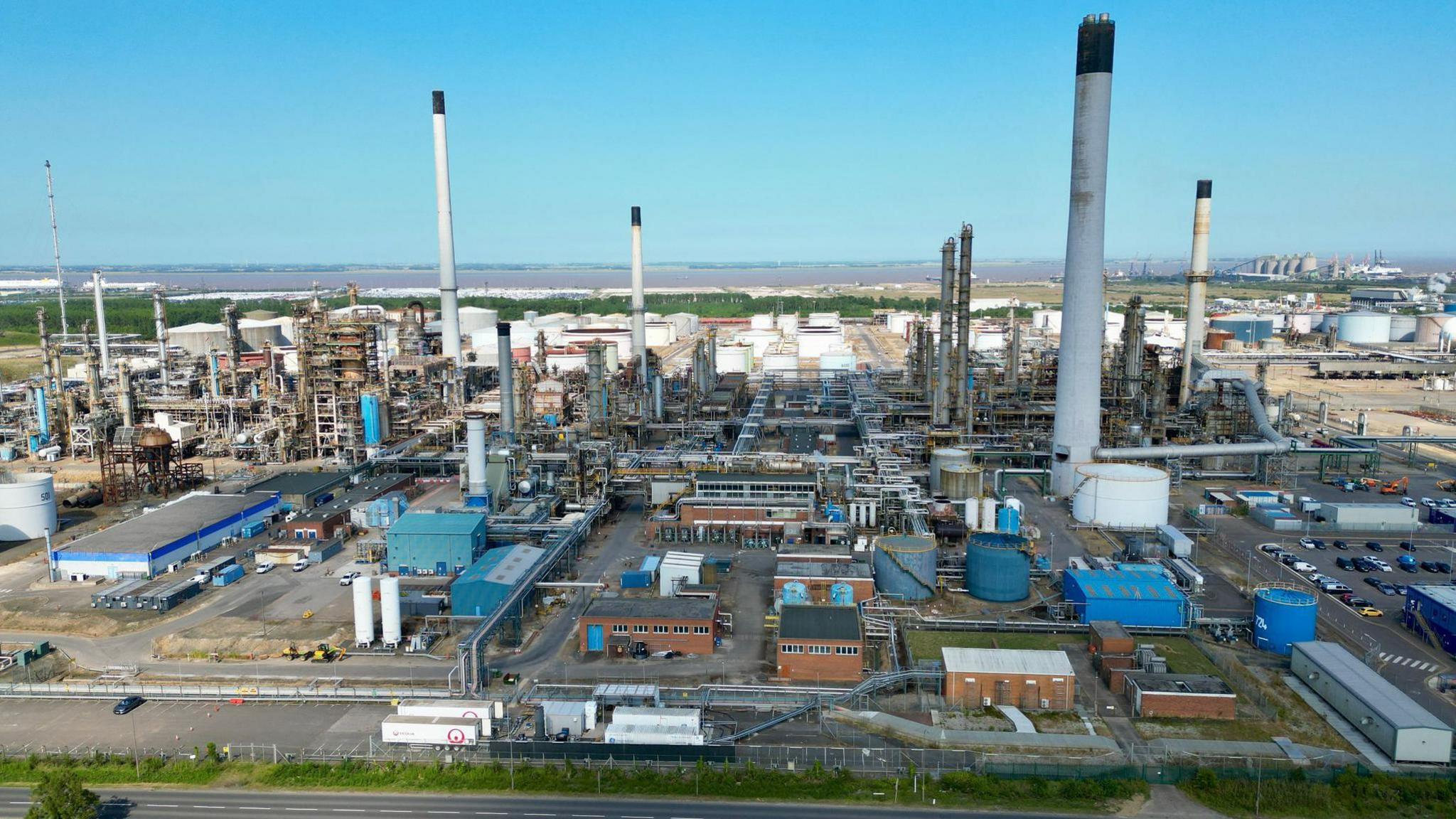 A drone view of the Prax Lindsey Oil Refinery. A cluster of metal structures rising to the blue sky.