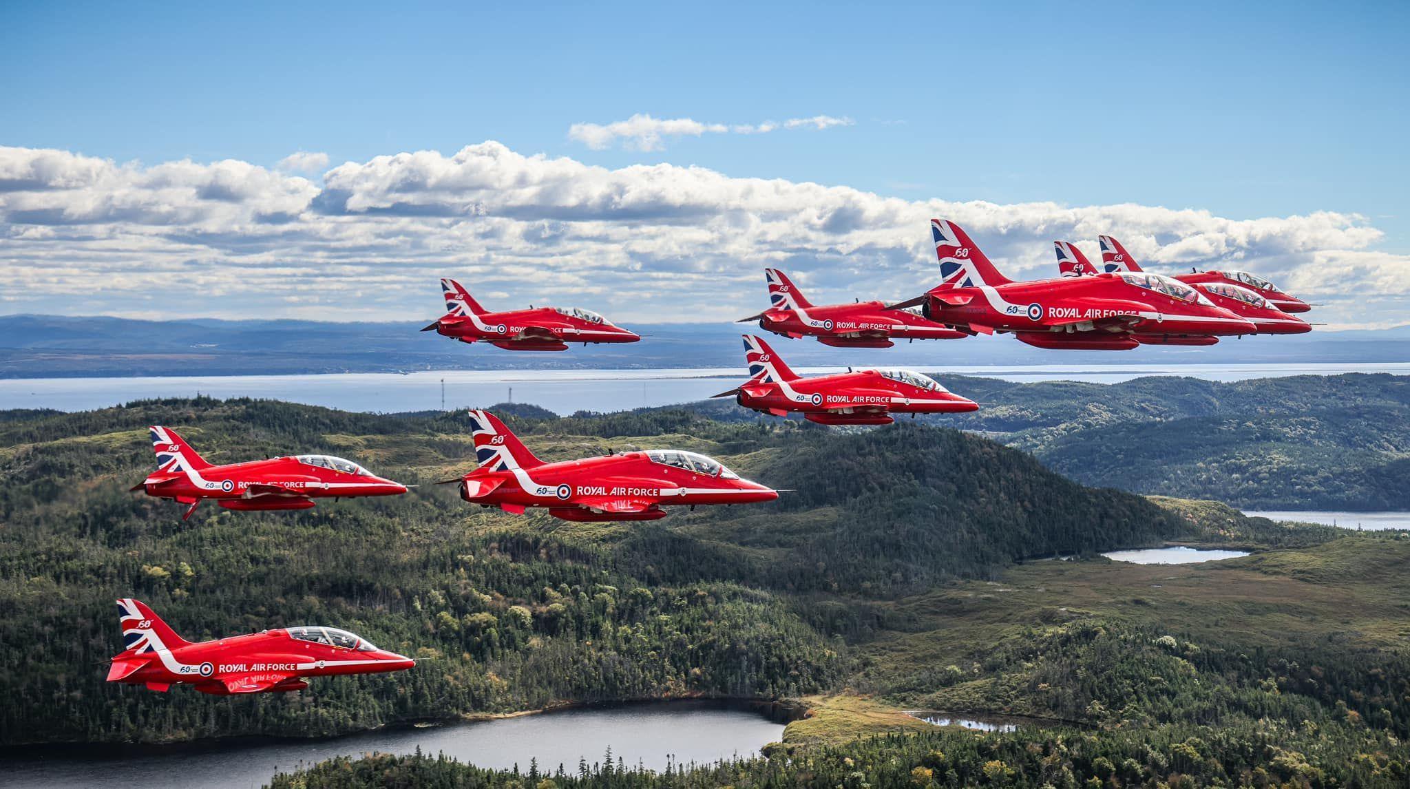 Red Arrows team flying over a vast Canadian landscape, carpeted with greenery. The team is in formation.